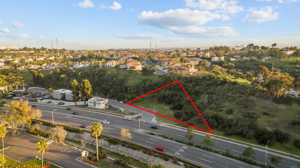 Undeveloped parcel outlined in red beside a multi-lane road, with homes in the background.