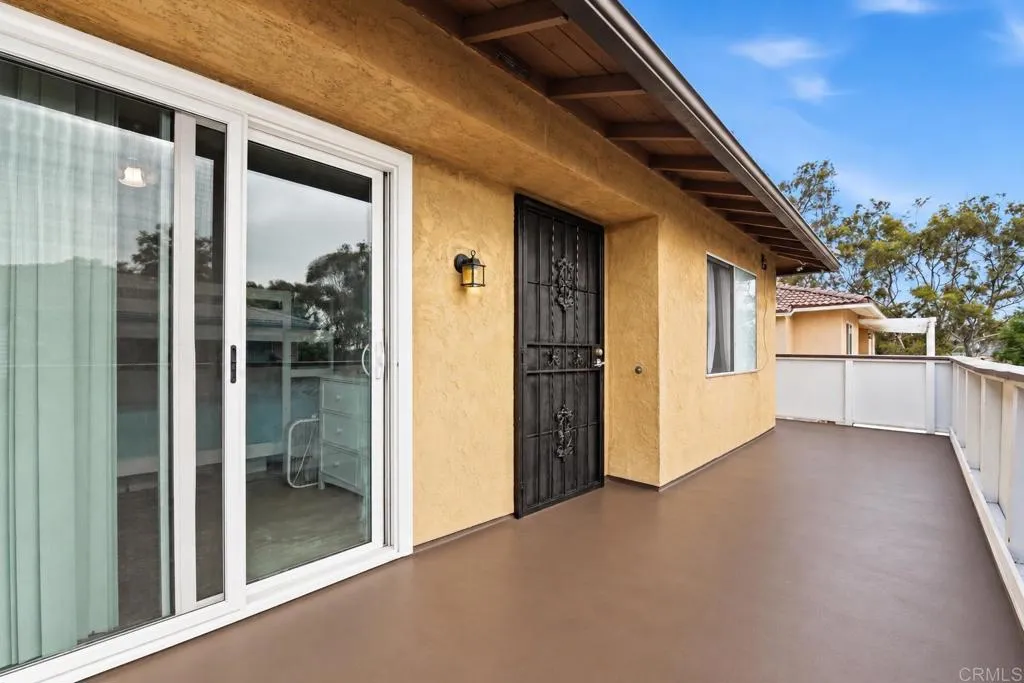 Home’s spacious raised patio with brown decking, white railing, sliding glass door, and decorative security door.