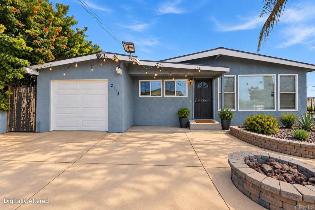 Blue-gray single-story home with a white garage, string lights, and a landscaped rock fire pit.