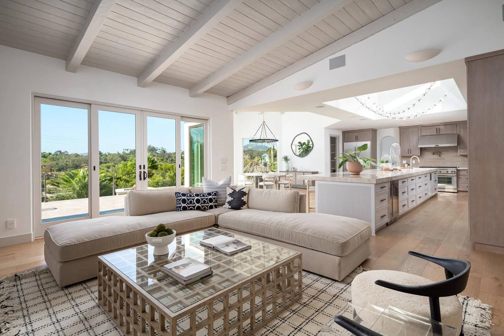 Open-plan living room and kitchen with vaulted ceiling, sectional sofa, and hillside views through sliding doors.