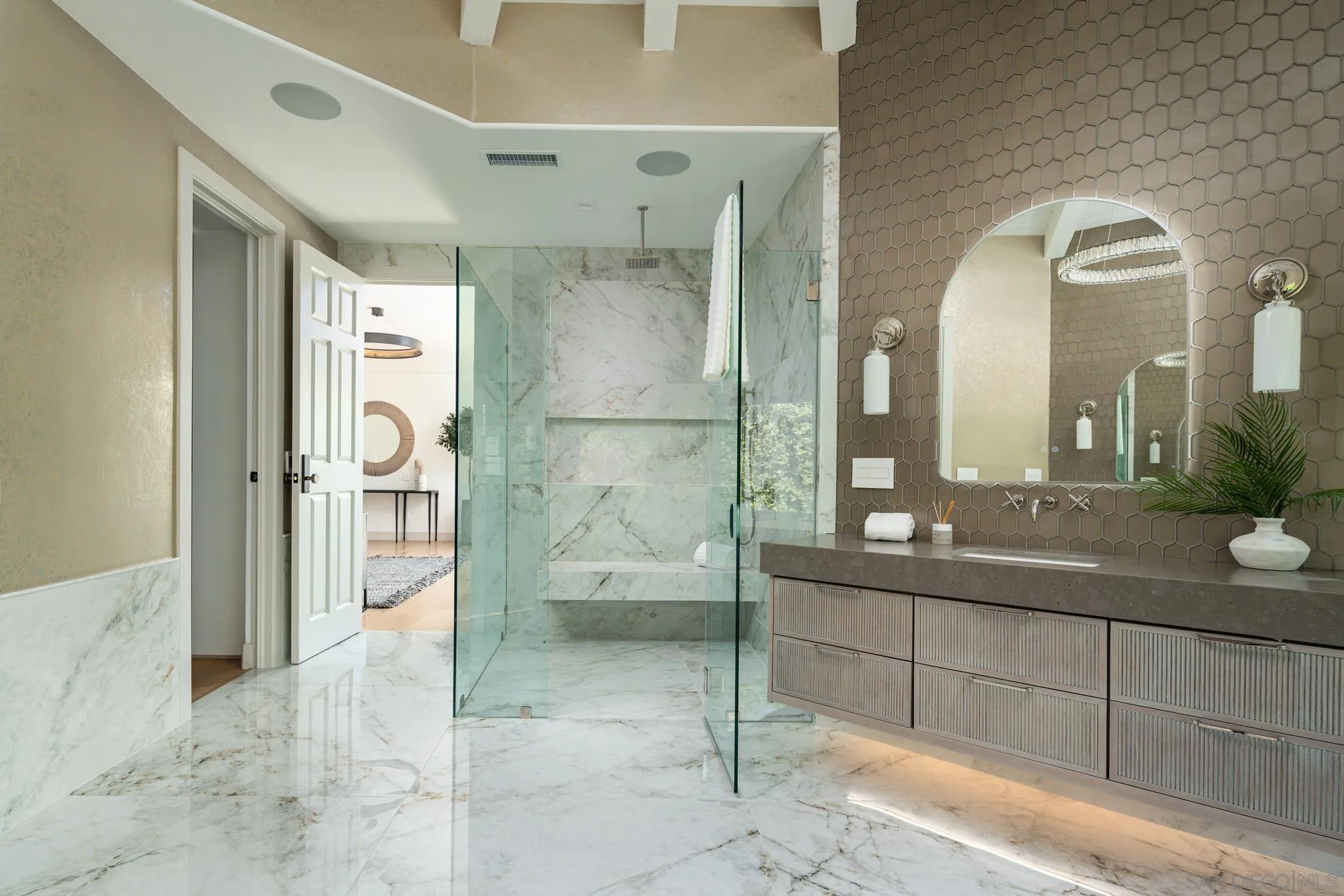 Bathroom with a marble walk-in shower, ribbed vanity, taupe hexagonal tile, and arched mirror.