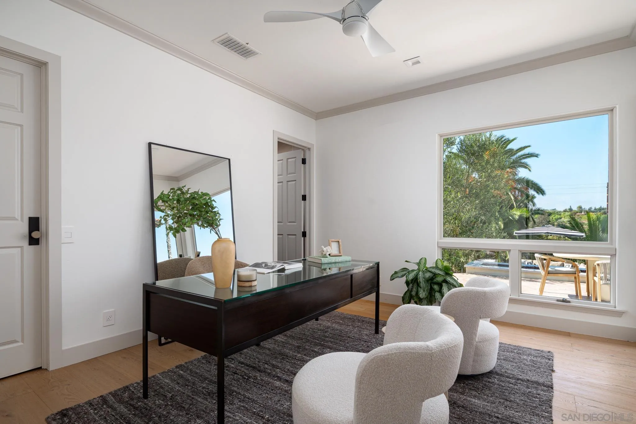 Staged home office with a glass-top desk and window overlooking trees and a poolside patio.