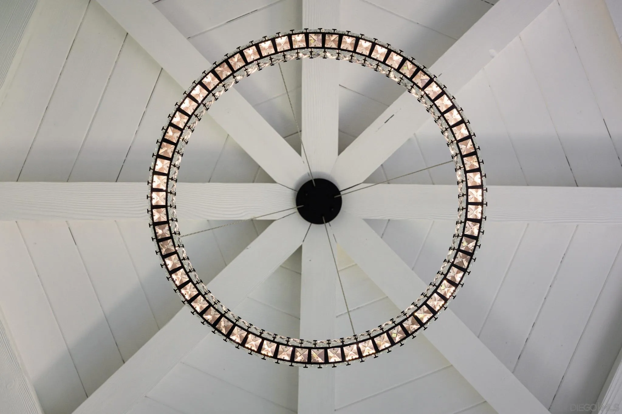 Circular crystal chandelier beneath a white vaulted ceiling with intersecting beams.