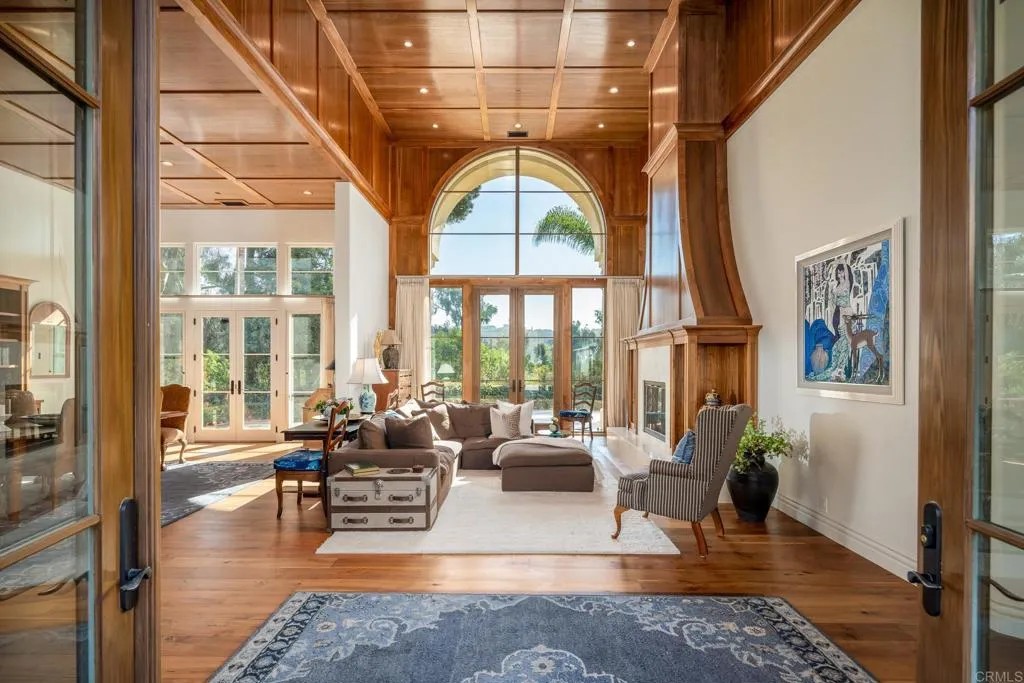 Living room with a high wood-paneled ceiling, arched window, and prominent wood-framed fireplace.