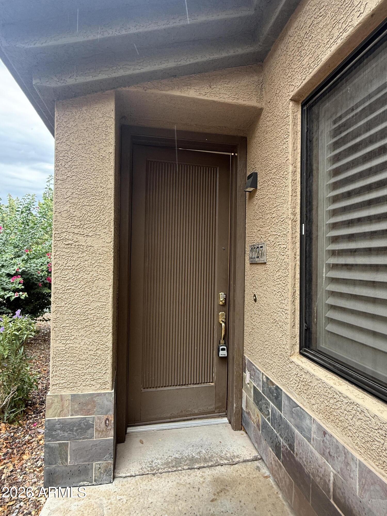 Recessed home entrance with a brown paneled door, unit number 1127, and tan stucco exterior.