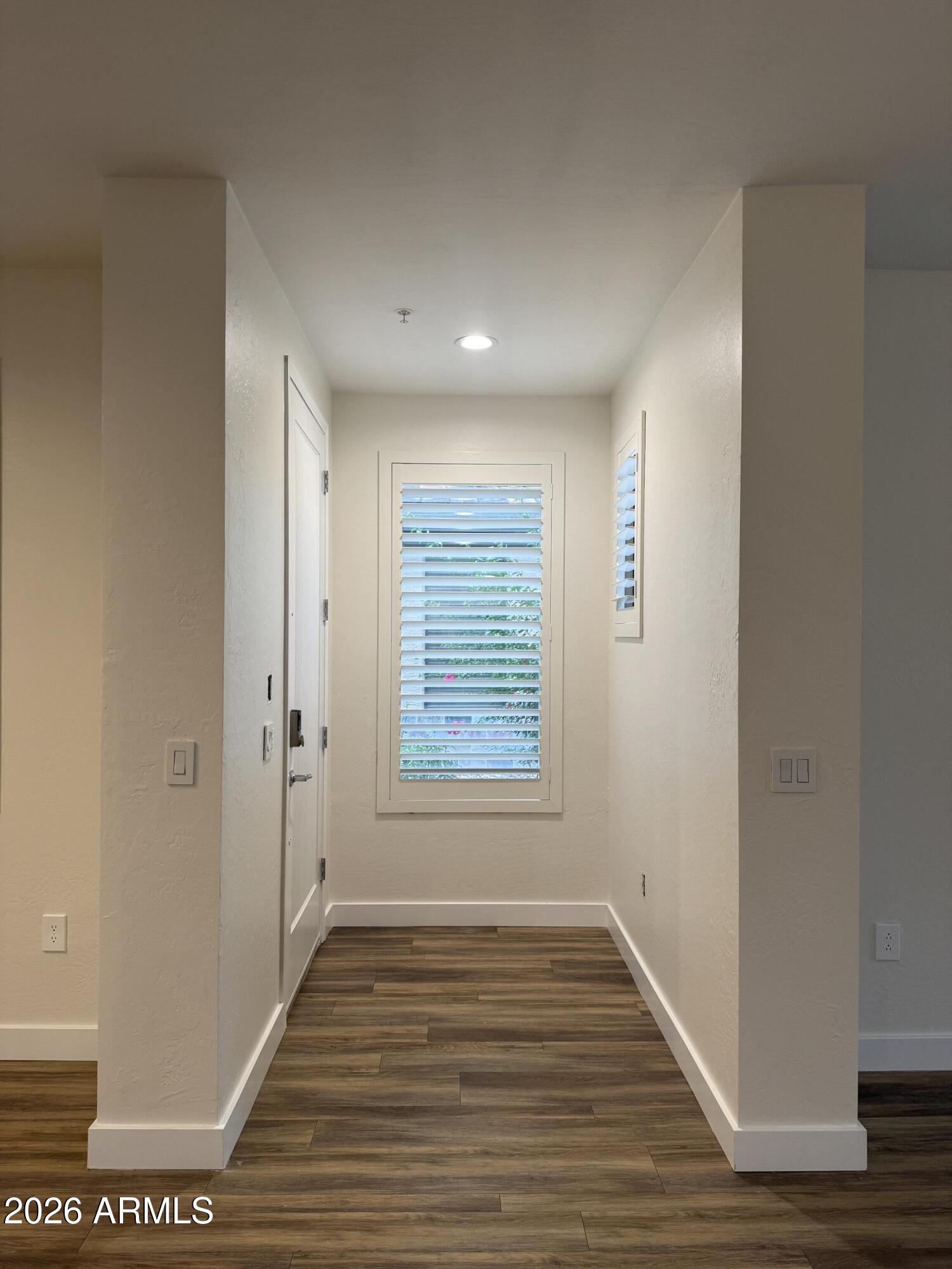 Entry hallway with wood-look floors, a white entry door, and plantation shutters on the windows.