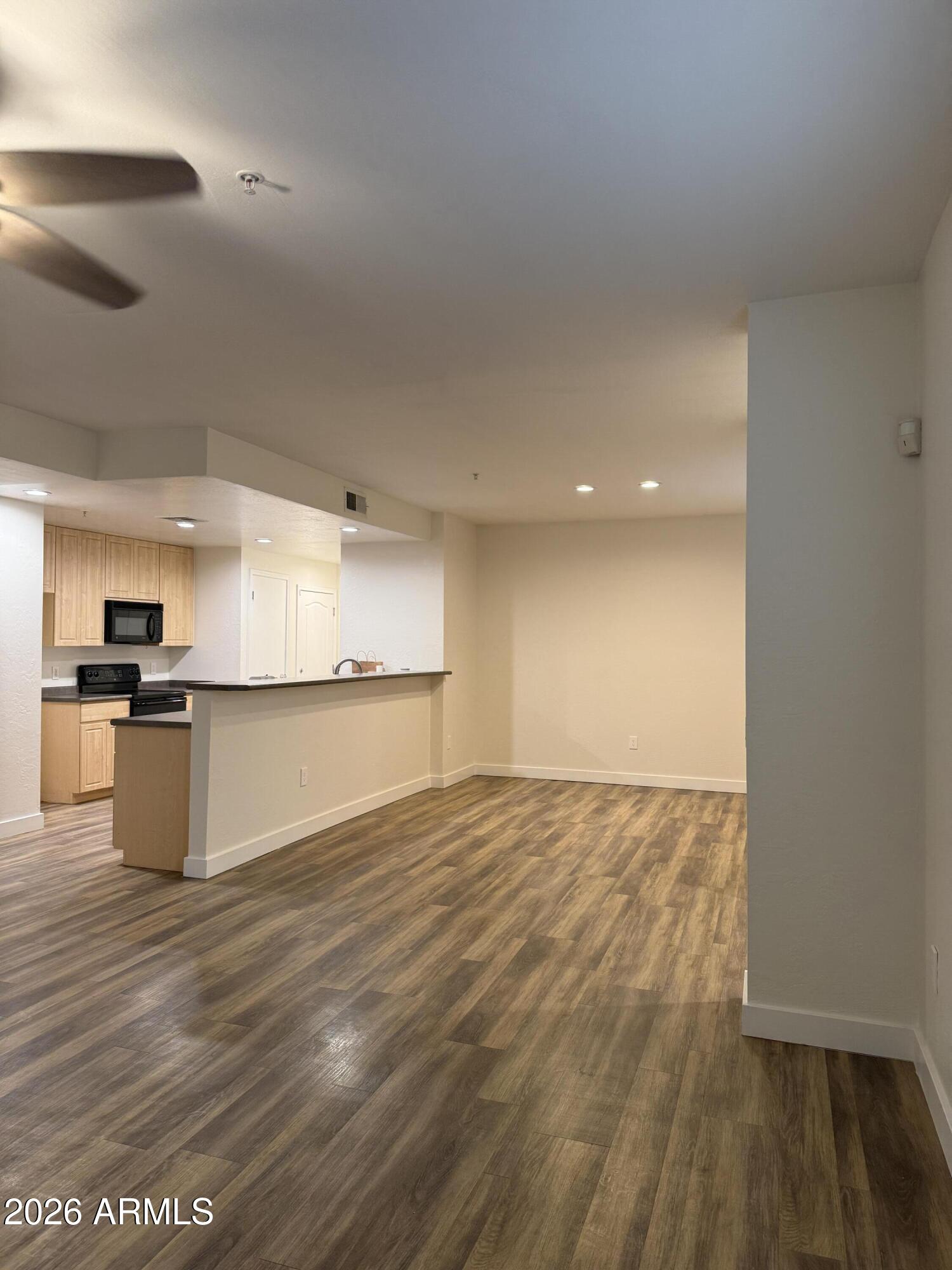 Vacant open-plan living area with wood-look flooring and a breakfast bar beside the kitchen.