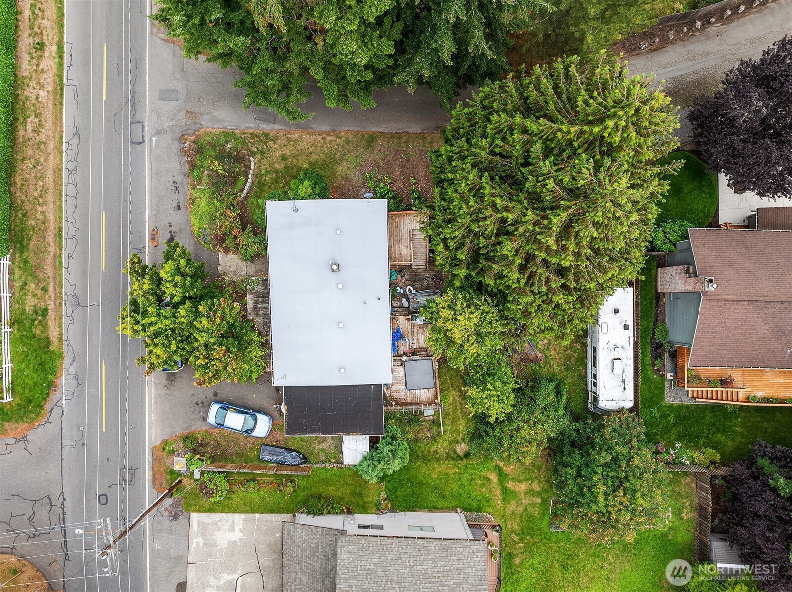 Aerial view of a house and landscaped lot beside a road, surrounded by mature trees.