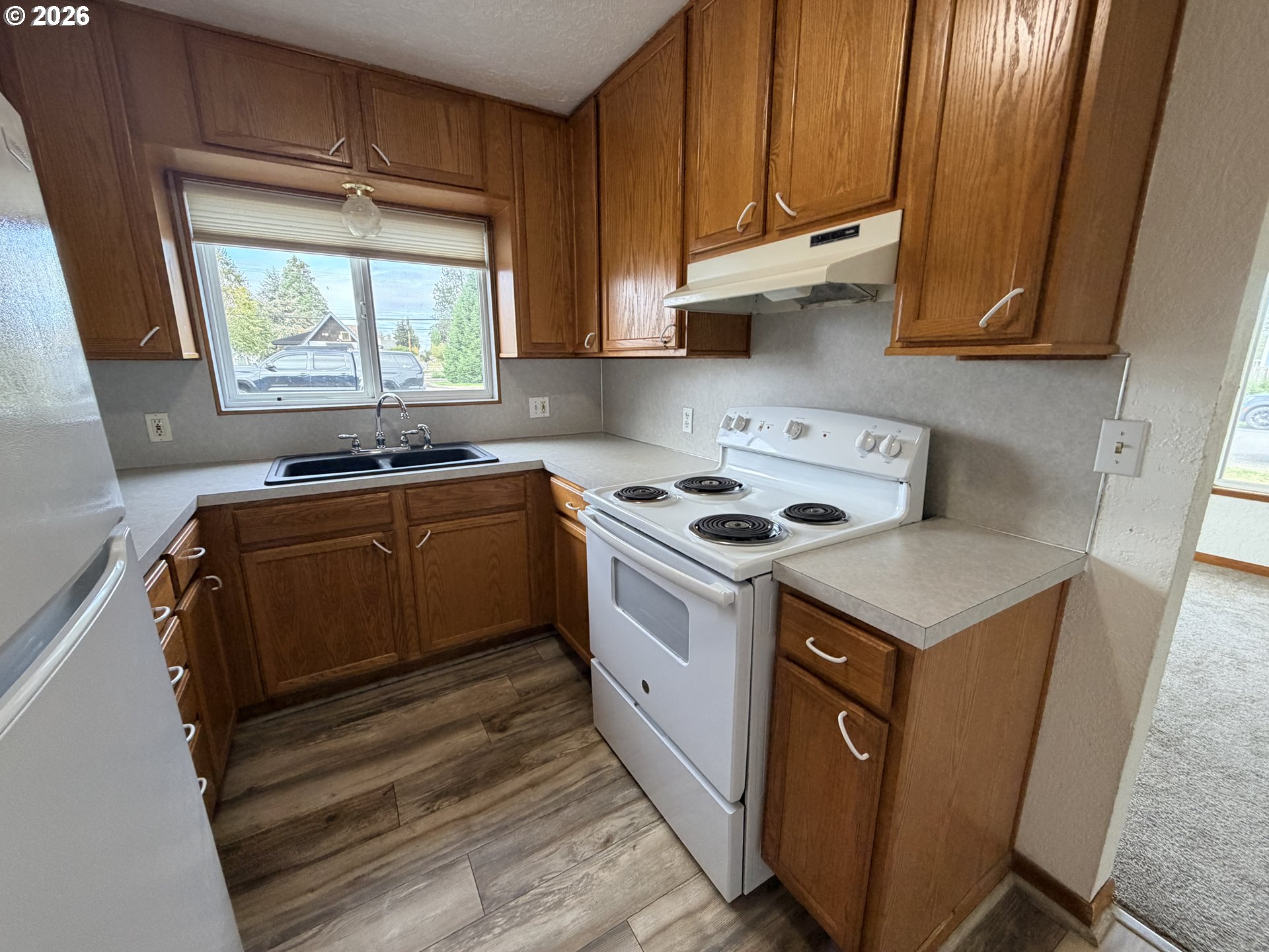 Kitchen with wood cabinets, a white electric range, and a sink beneath a window.