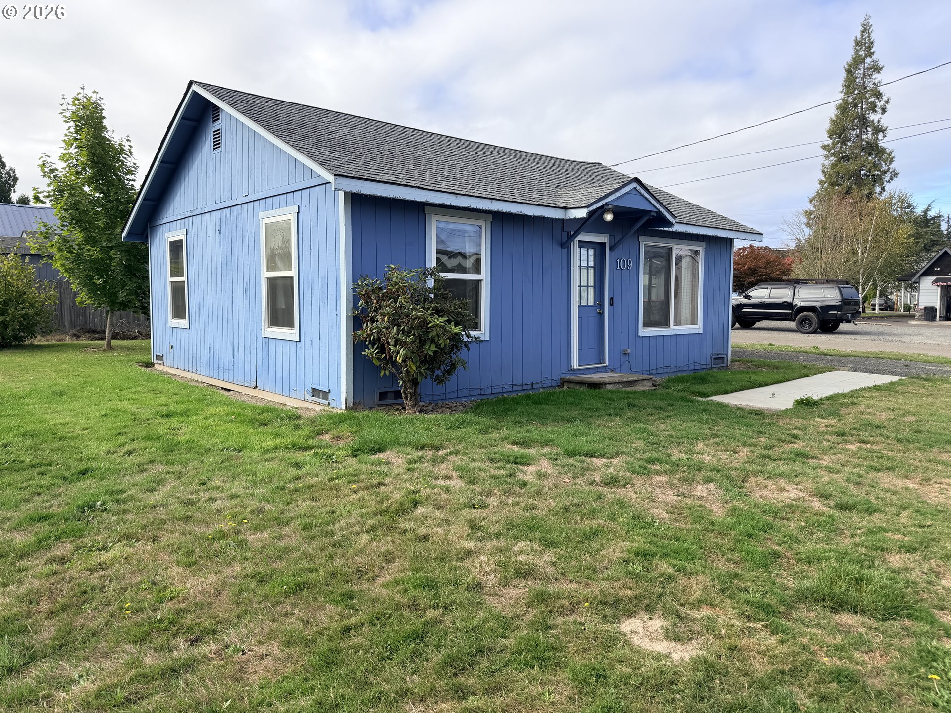 Blue single-story house with white-trimmed windows, a gabled roof, and a front lawn.