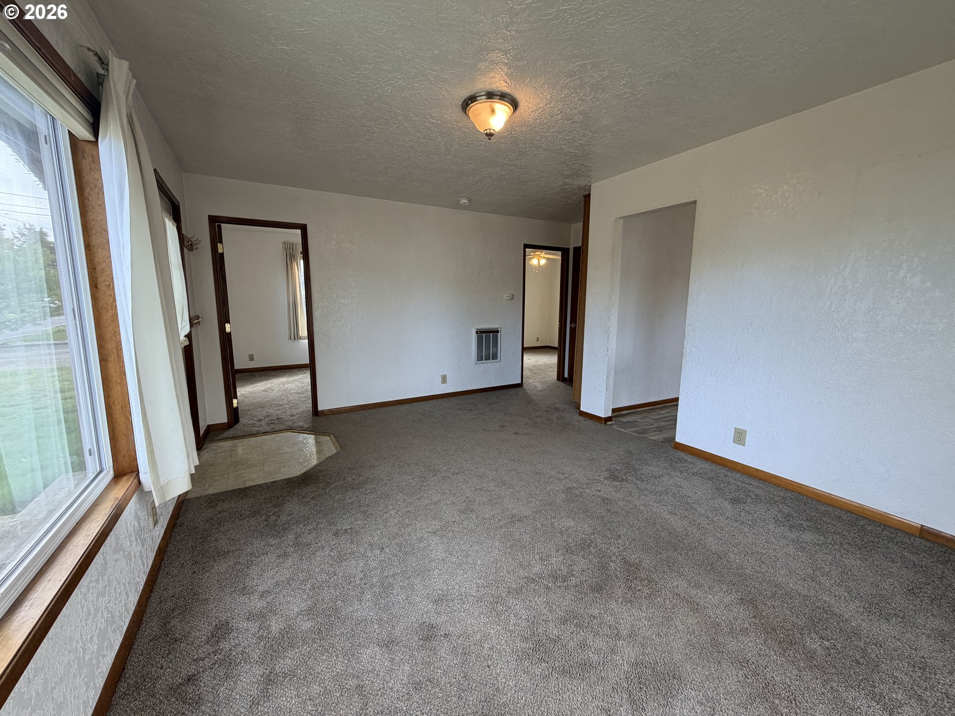 Vacant carpeted living room with a large window and doorways to adjoining rooms.