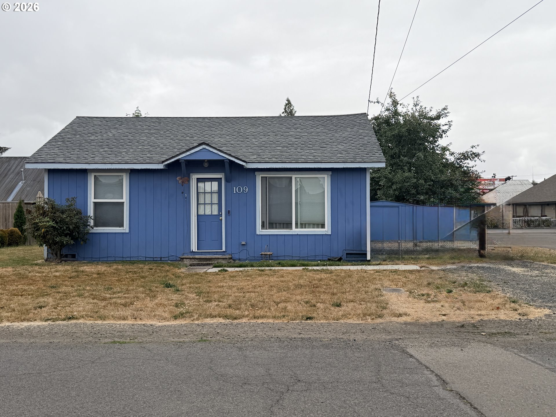 Blue single-story house with white-trimmed windows, a blue entry door, and gray shingle roof.
