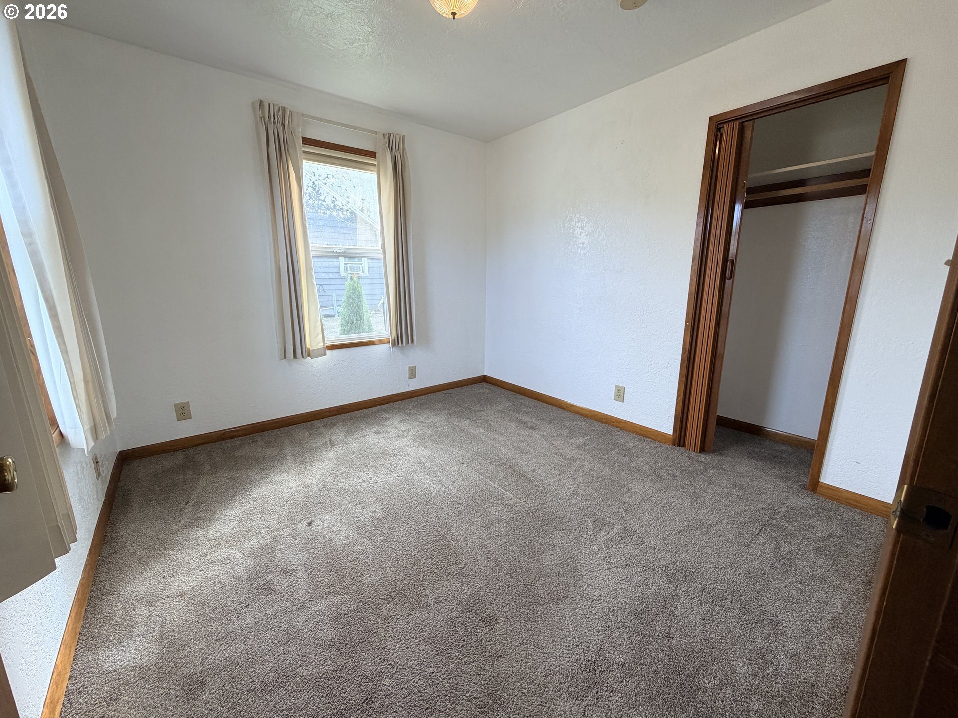 Empty carpeted room with a curtained window and open closet.