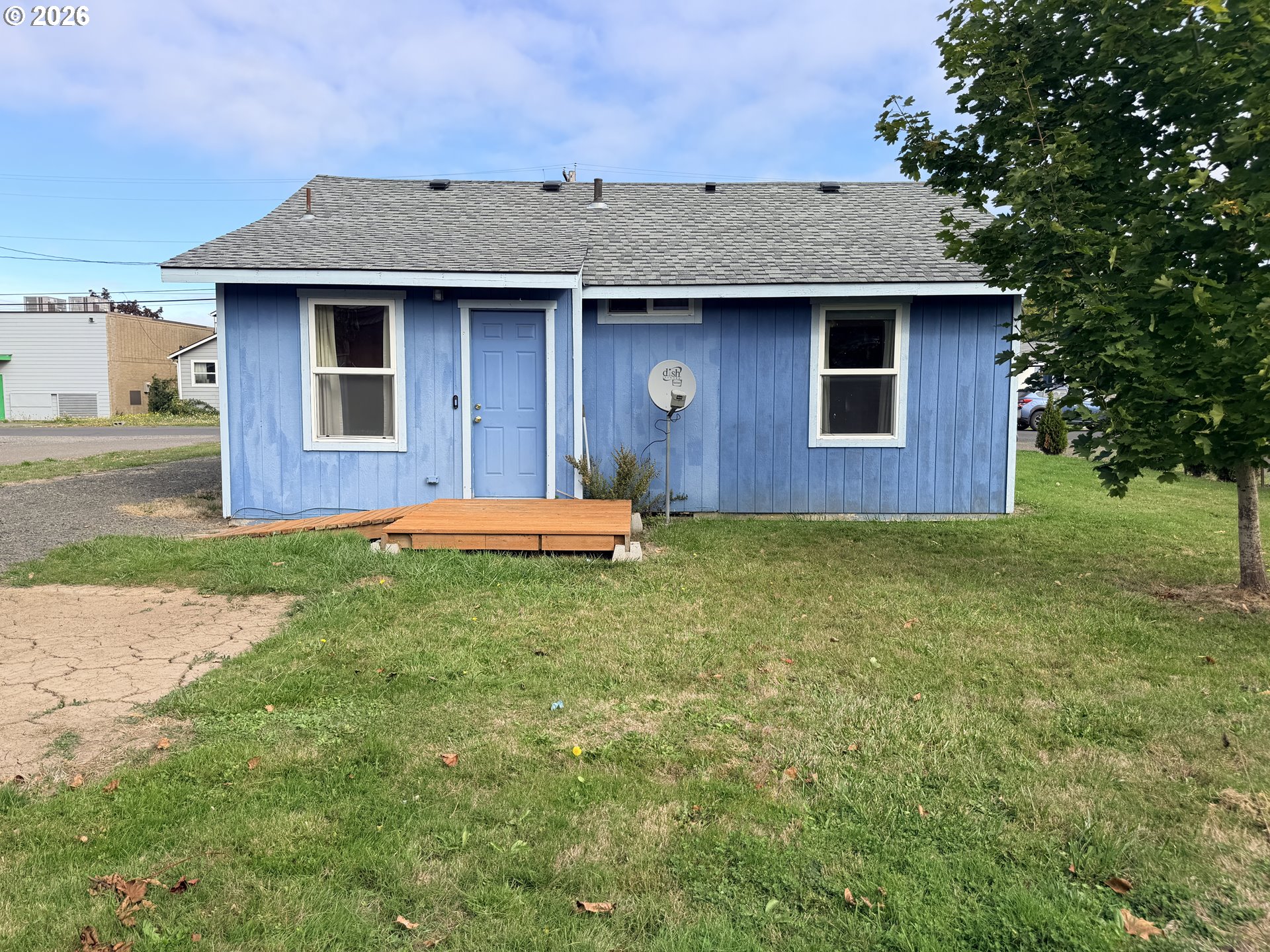 Blue house exterior with white trim, a small wooden deck, and a large tree beside the lawn.