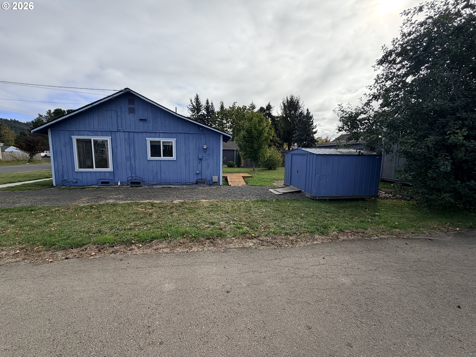 Blue house with white-trimmed windows and a matching shed beside the gravel driveway.