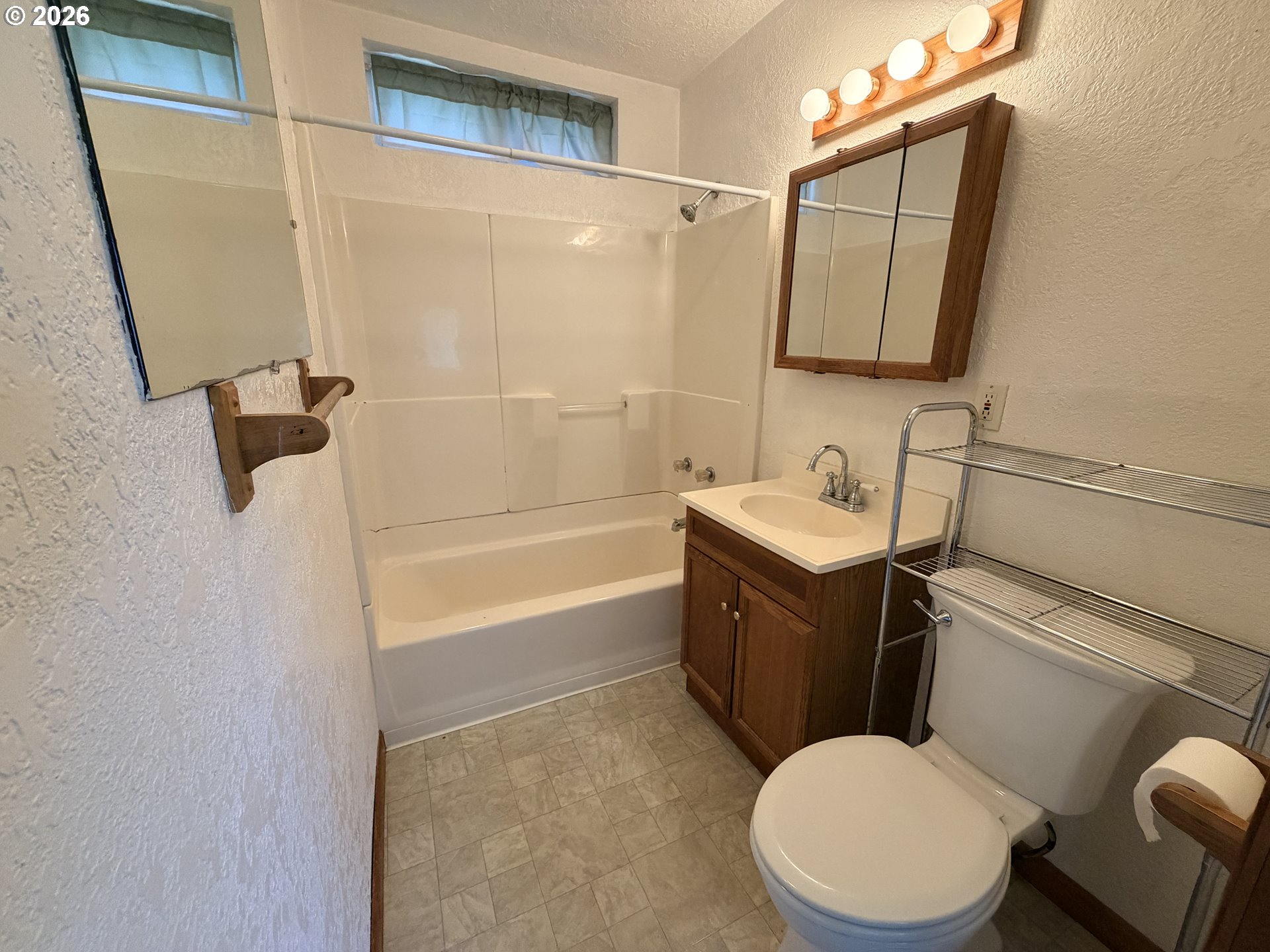 Bathroom with a tub and shower, wood vanity, mirrored cabinet, and high windows.