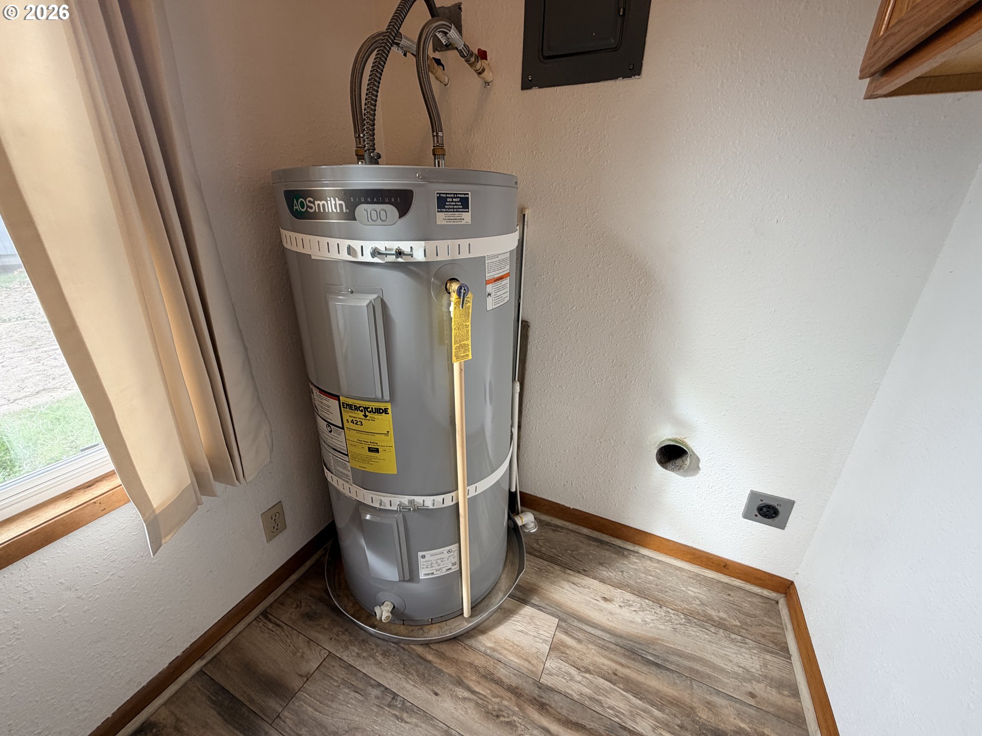 Water heater in a small utility area beside a window and wood-look flooring.