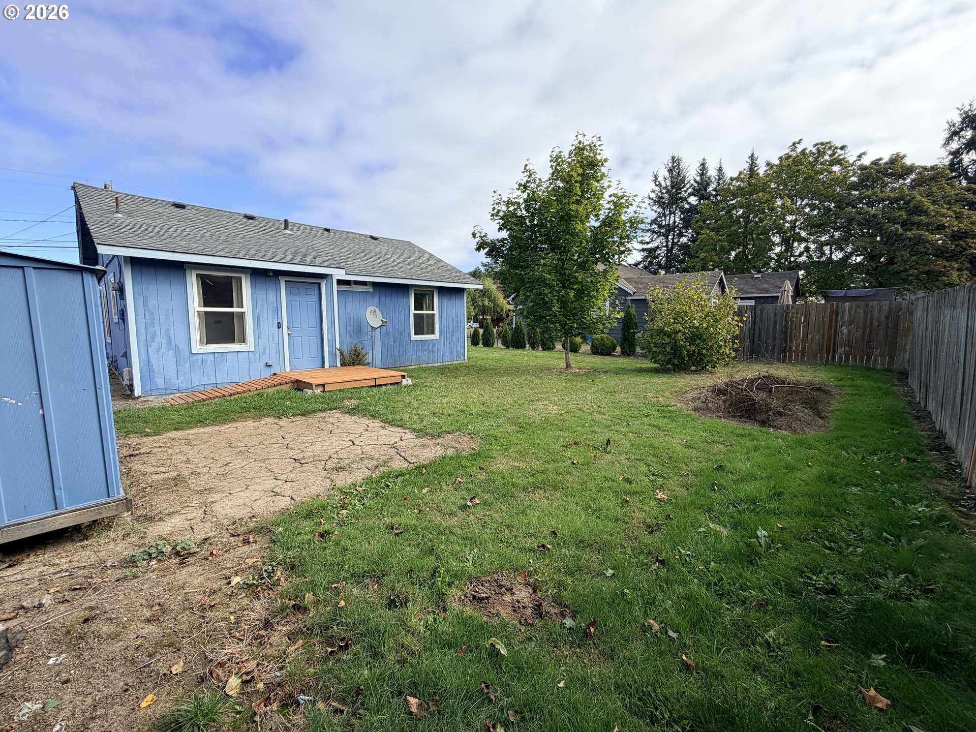 Blue house with a fenced grassy backyard, small deck, shed, and concrete patio.