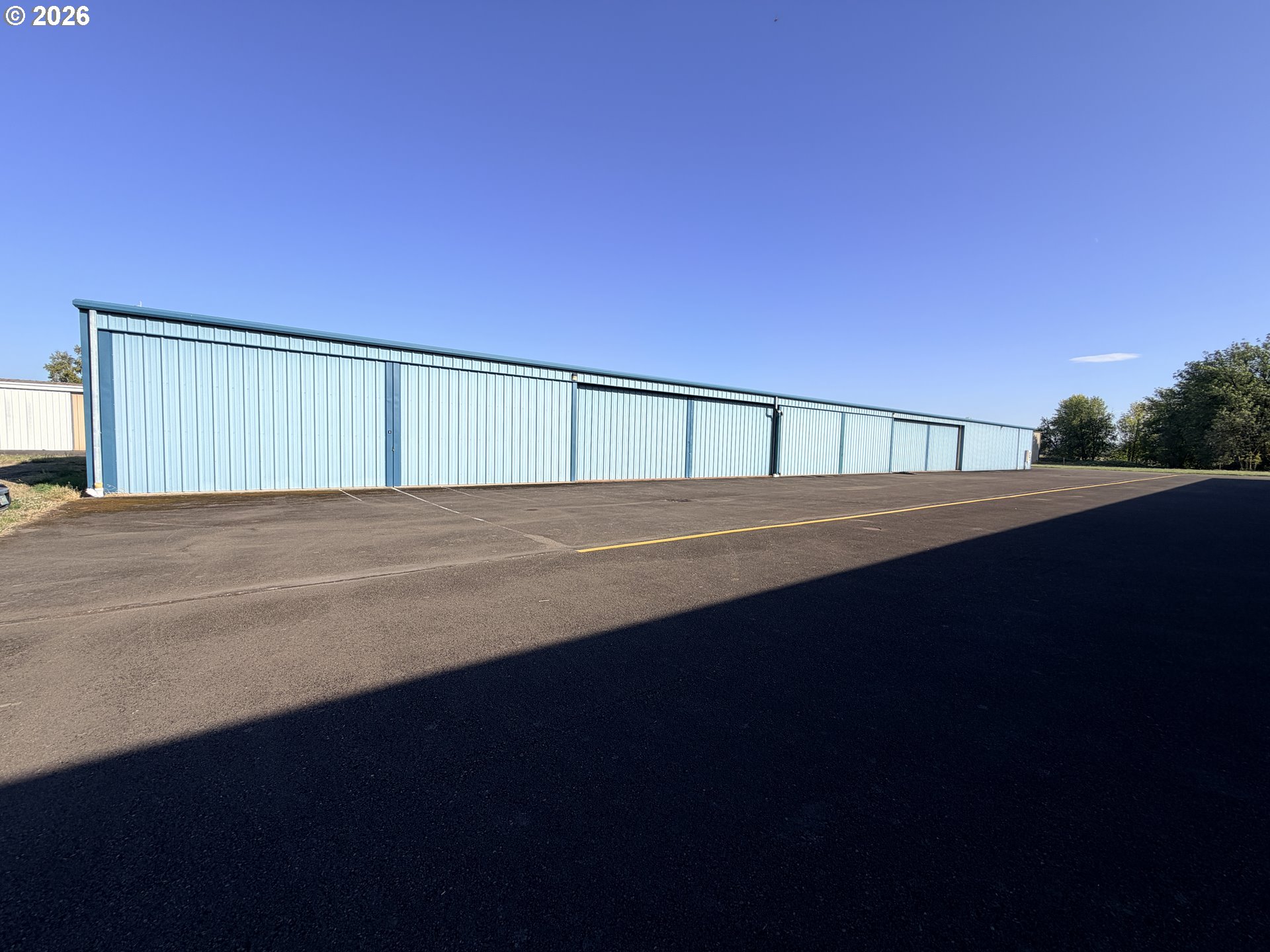 Long light-blue metal aircraft hangar with multiple doors and a wide paved apron.
