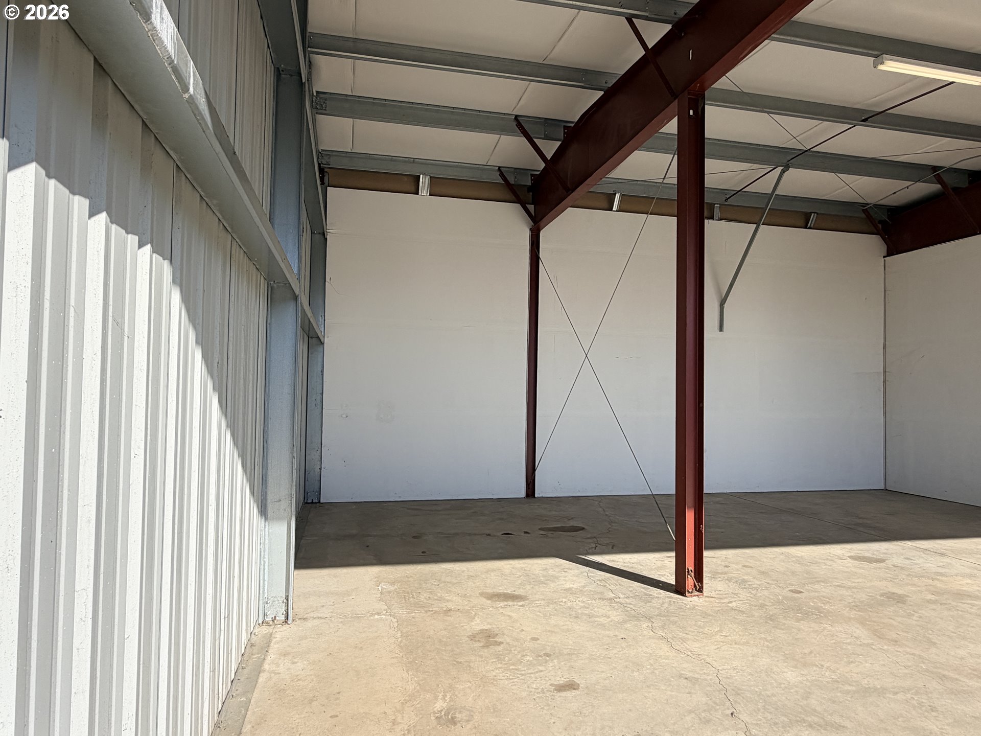 Empty airport hangar with a concrete floor, corrugated walls, and exposed red steel supports.