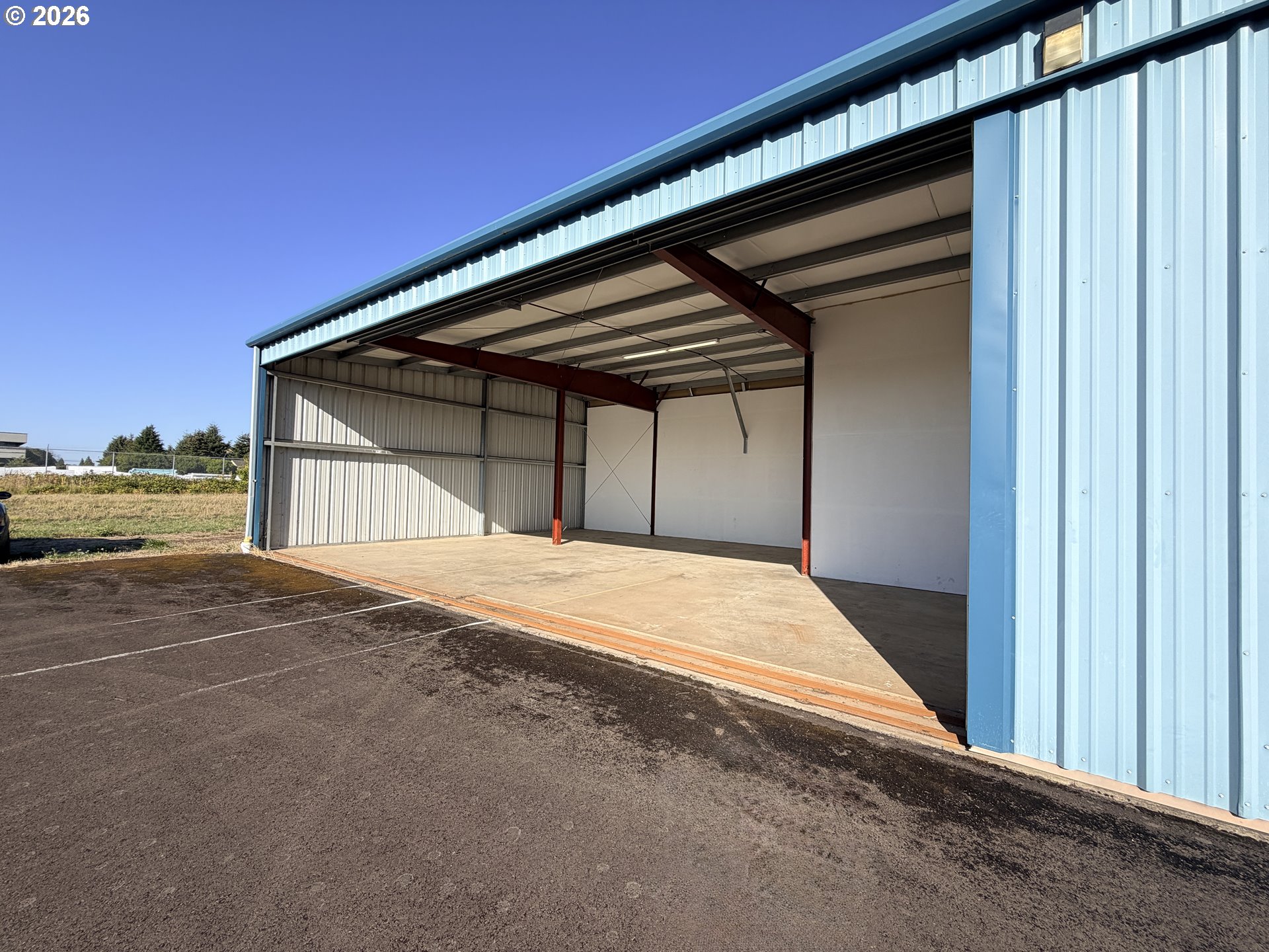 Open blue metal aircraft hangar with exposed steel supports and an empty concrete floor.