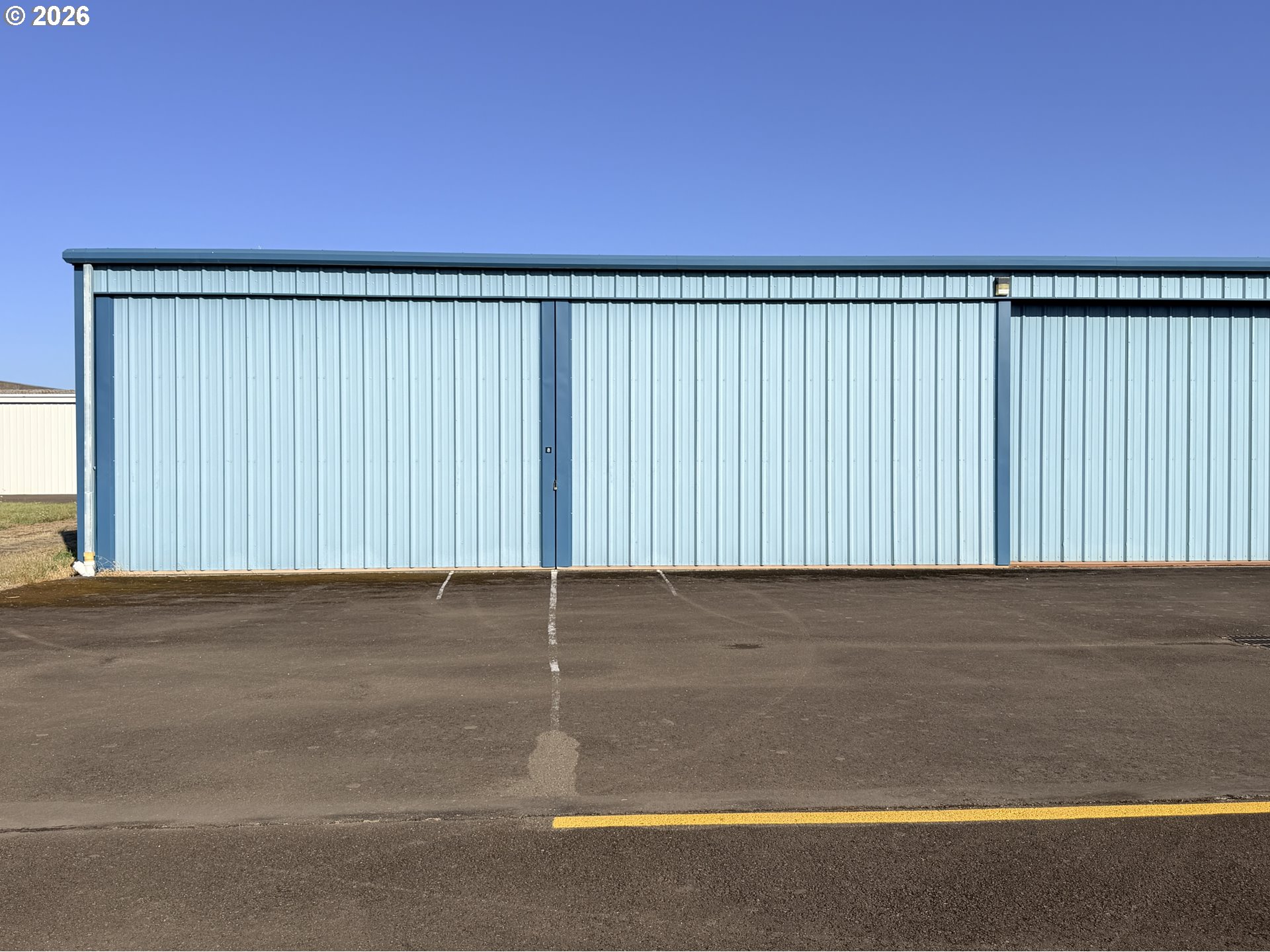 Light-blue metal aircraft hangar with a narrow door marked 8 and an asphalt apron.