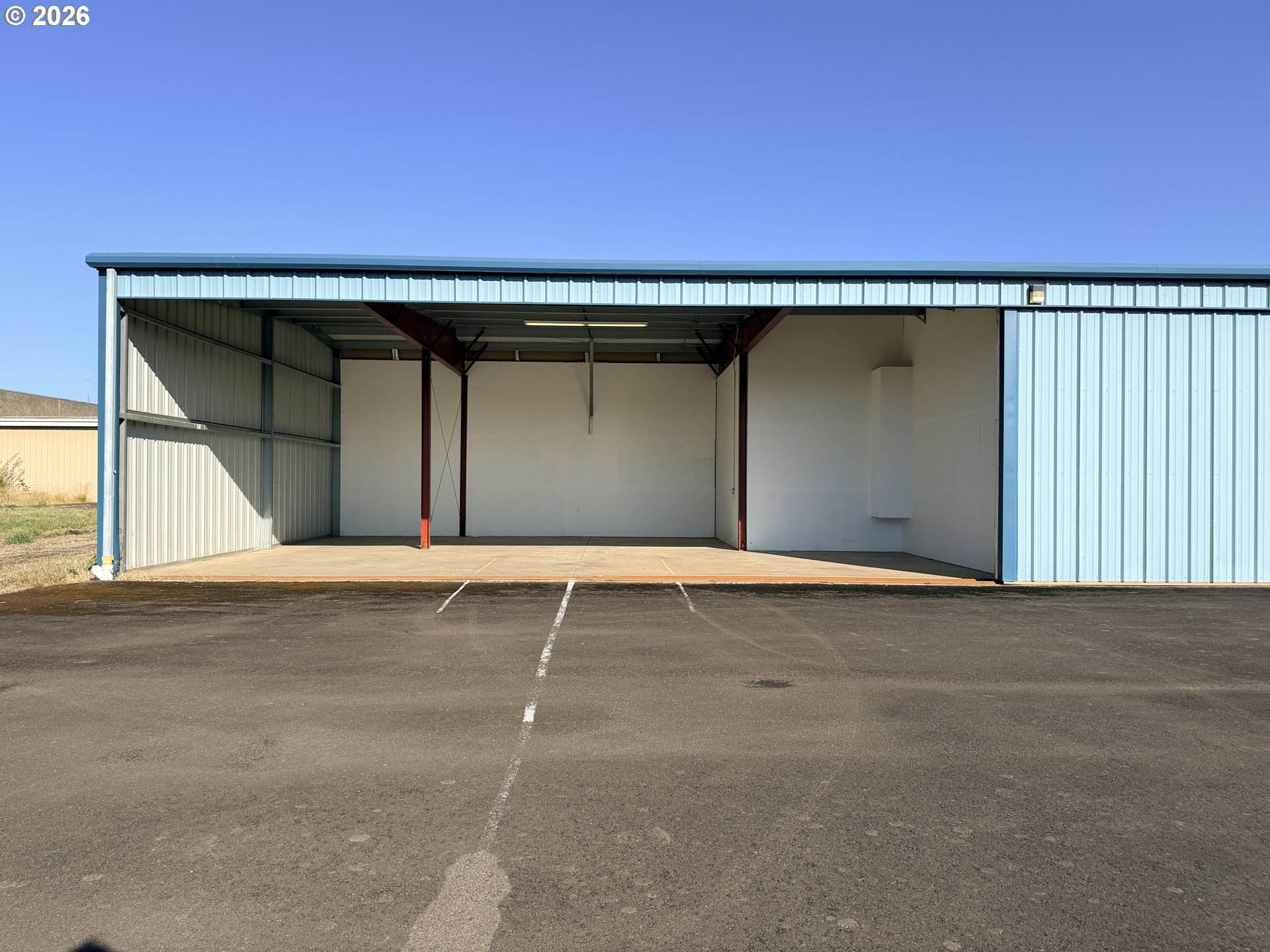 Open-front metal aircraft hangar with blue siding and parking spaces on the asphalt apron.