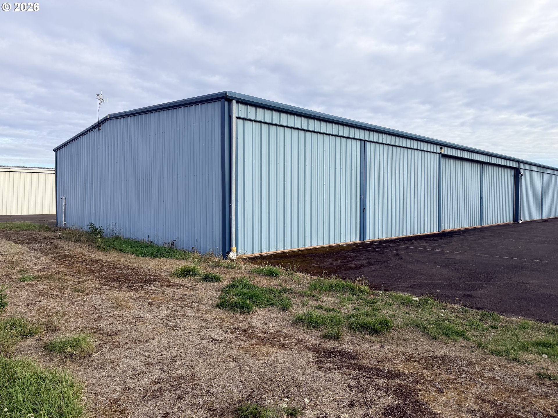 Blue-gray metal airport hangar with large sliding doors and an asphalt apron.