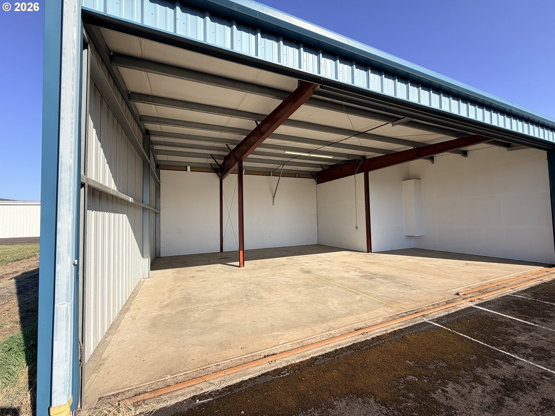 Empty aircraft hangar with an open bay door, exposed steel beams, and a concrete floor.