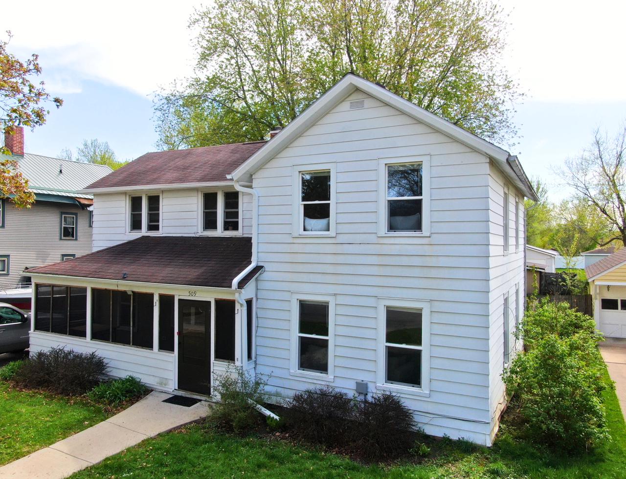 White two-story house with an enclosed front porch and red-brown roof, viewed from the front.