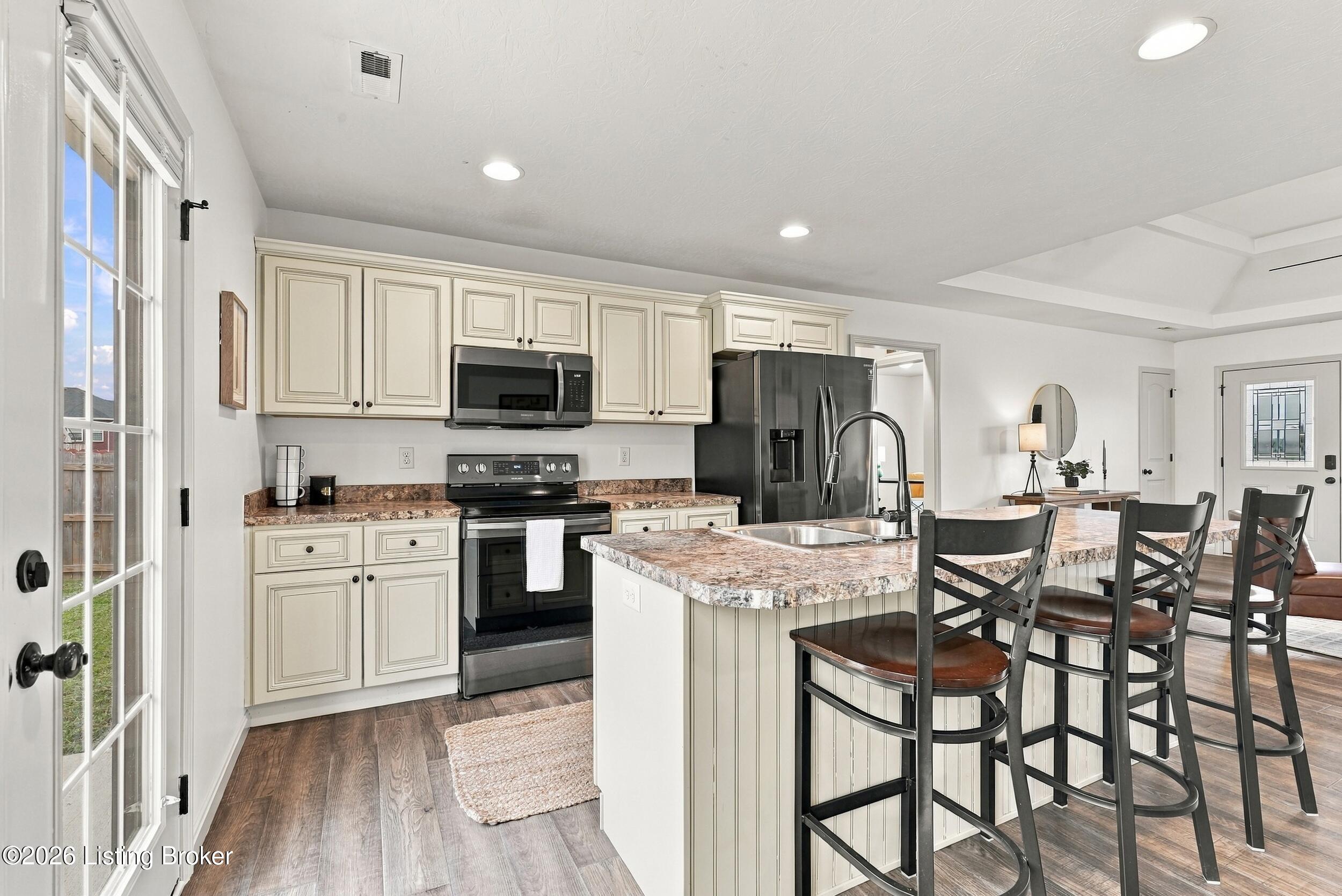 Kitchen with cream cabinets, stainless steel appliances, and a granite island lined with dark bar stools.