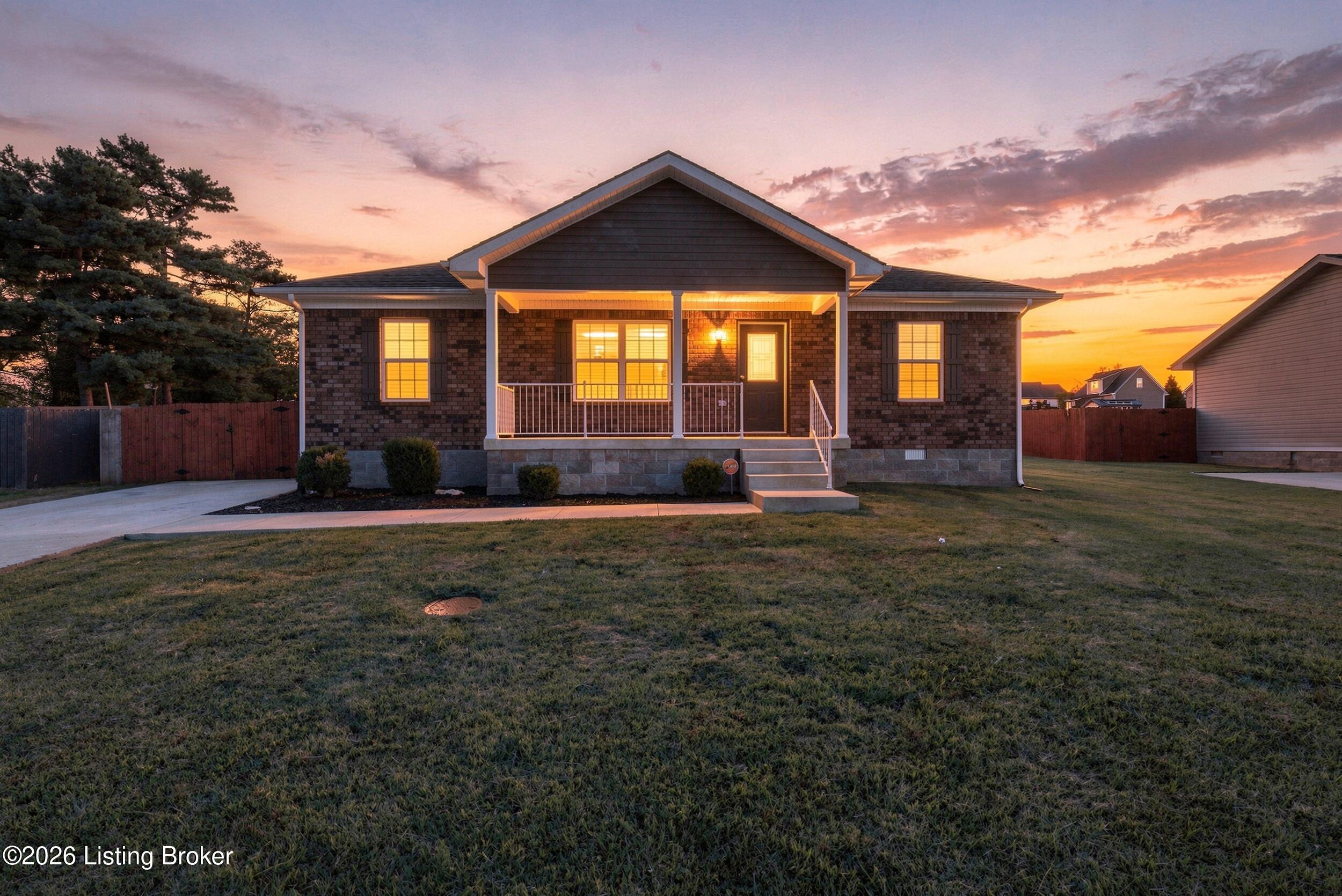 Brick home at dusk with a covered porch, glowing windows, and a broad front lawn.
