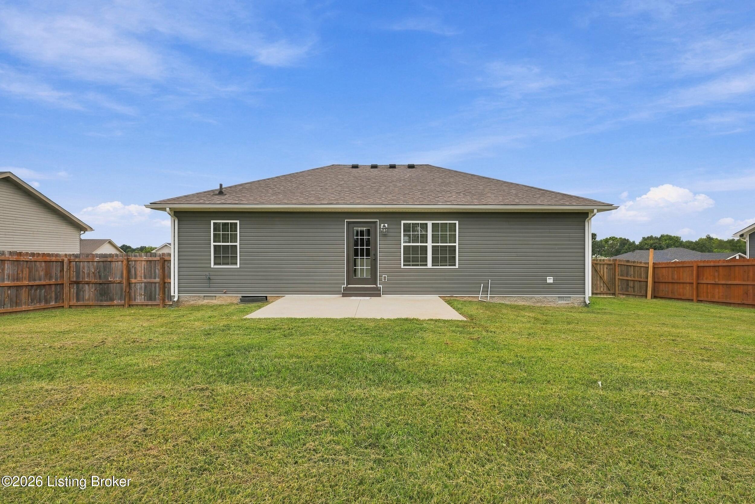 Rear of a gray-sided home with a concrete patio, broad grassy yard, and wooden privacy fence.