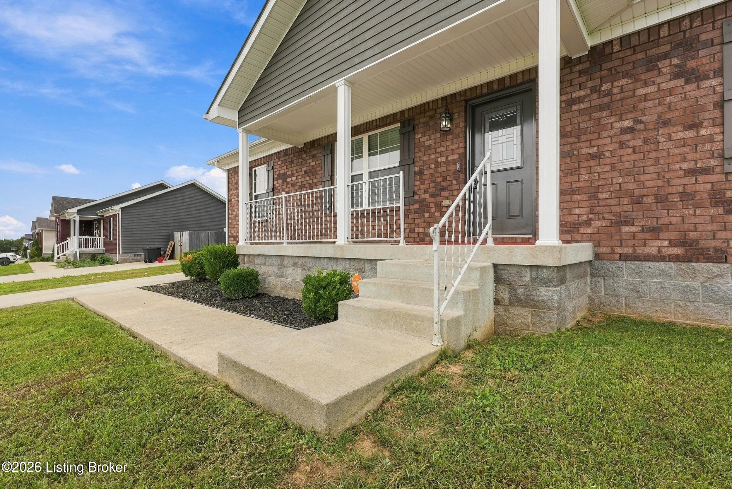 Brick home with a covered front porch, white railings, and concrete steps.