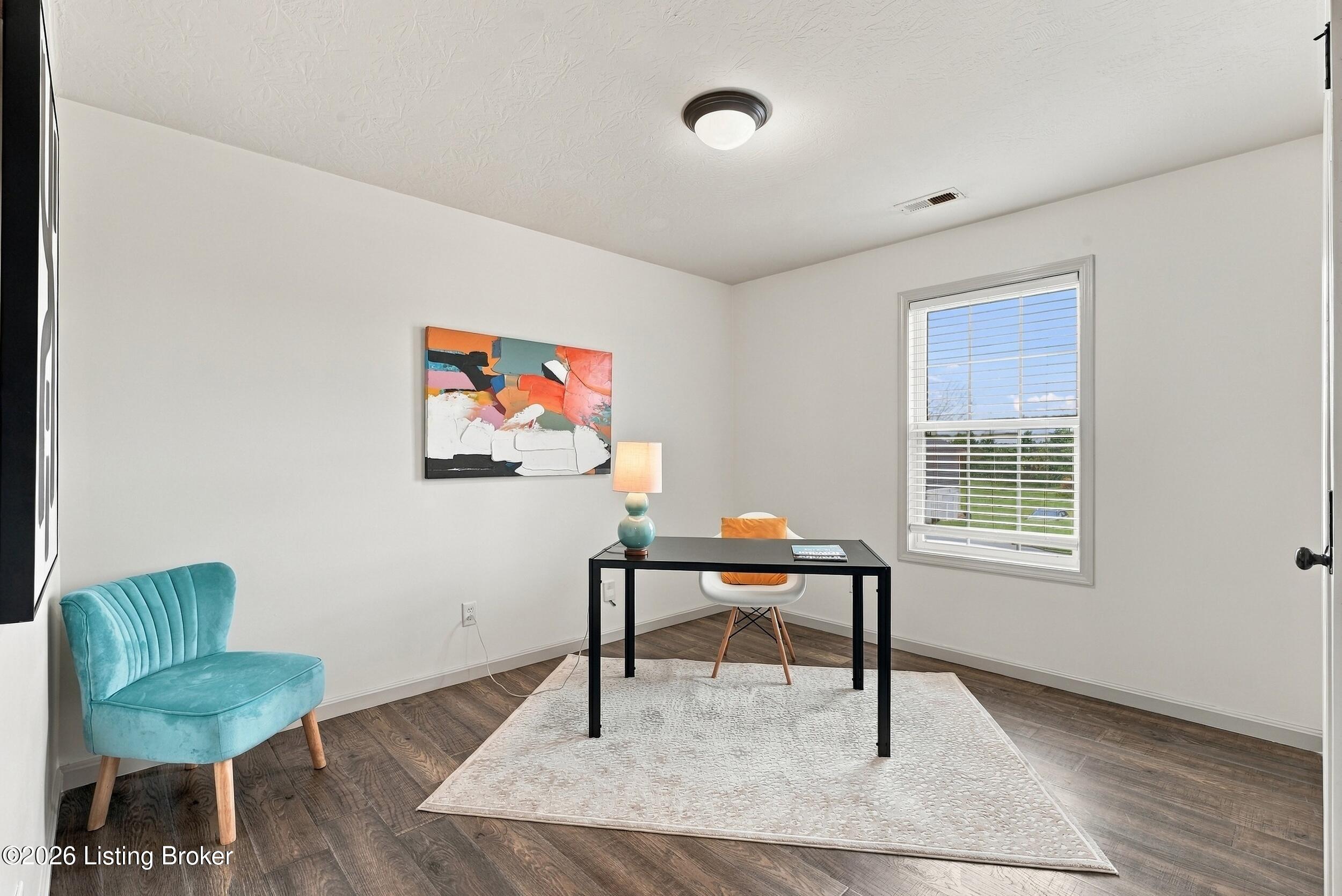 Furnished home office with a black desk, turquoise chair, abstract artwork, and a window with blinds.