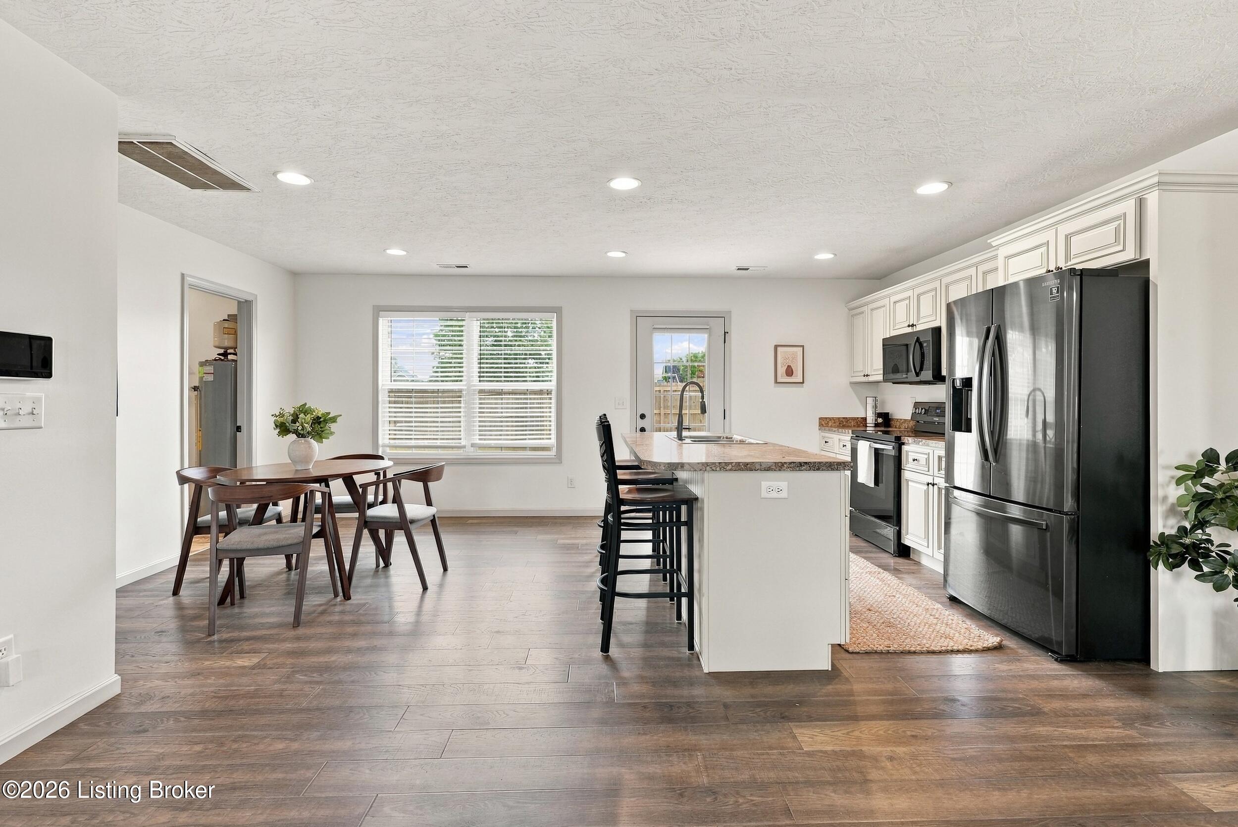 Open kitchen with white cabinets, stainless appliances, a large island, and an adjoining dining area.