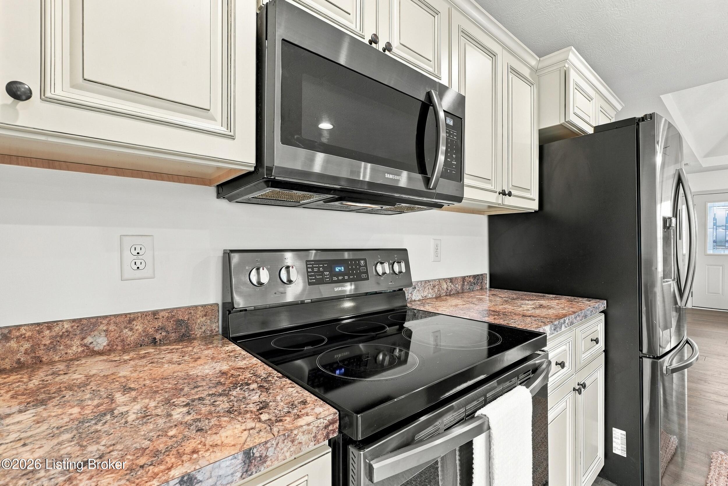Kitchen with white cabinets, mottled counters, and black-and-stainless appliances.