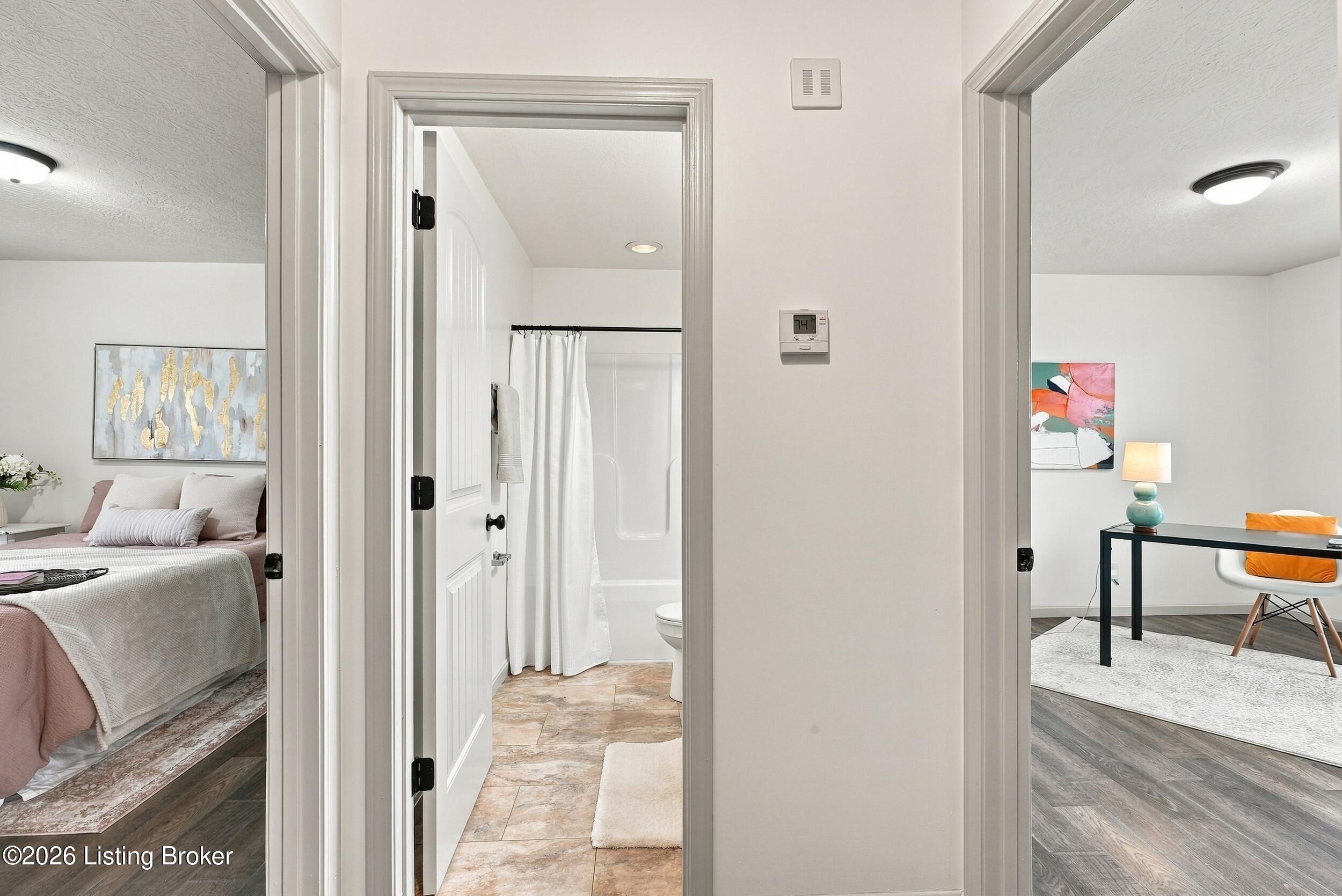 Bathroom doorway between a bedroom and office, with a white shower curtain and tiled floor.