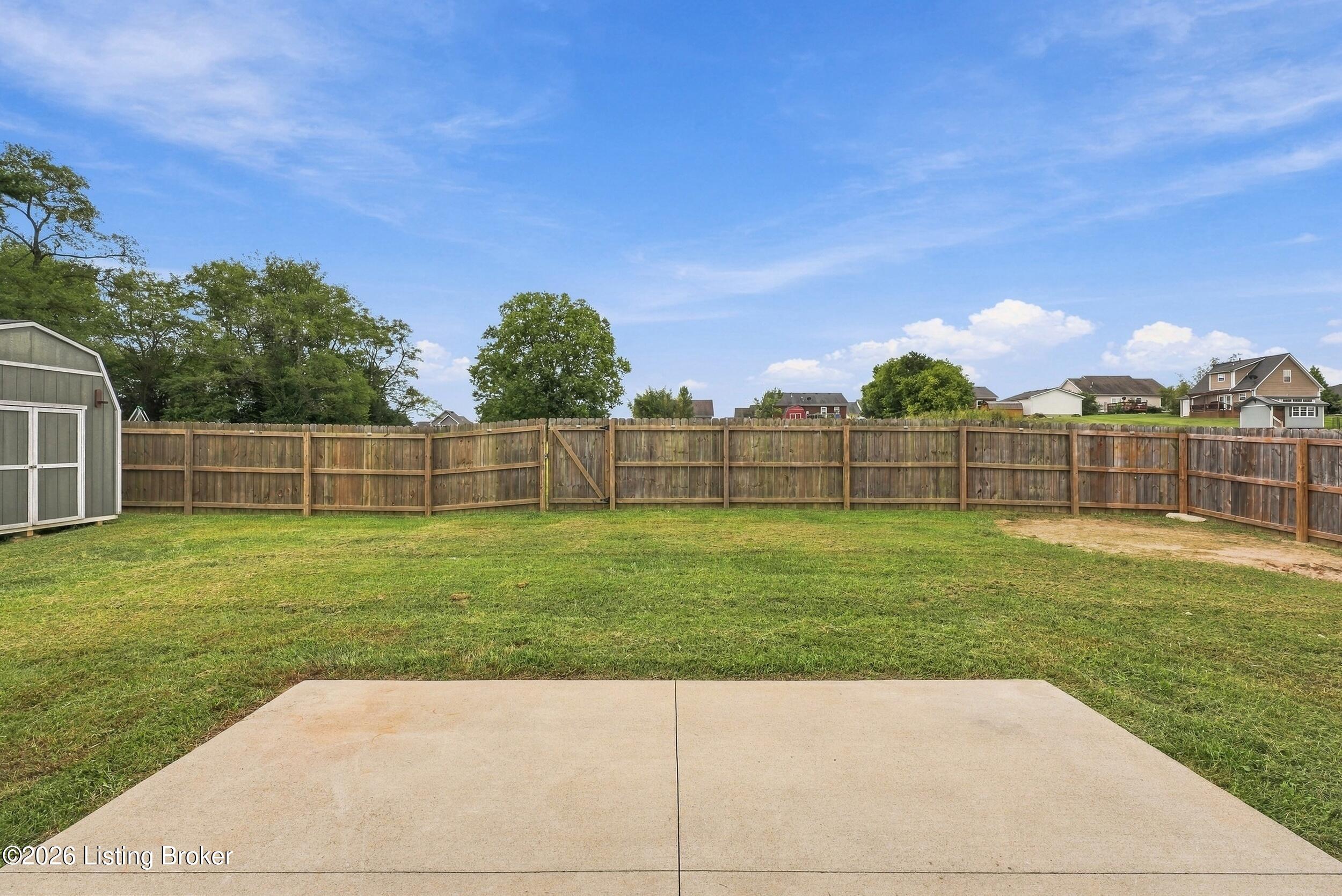 Fenced backyard with a concrete patio, lawn, and storage shed.