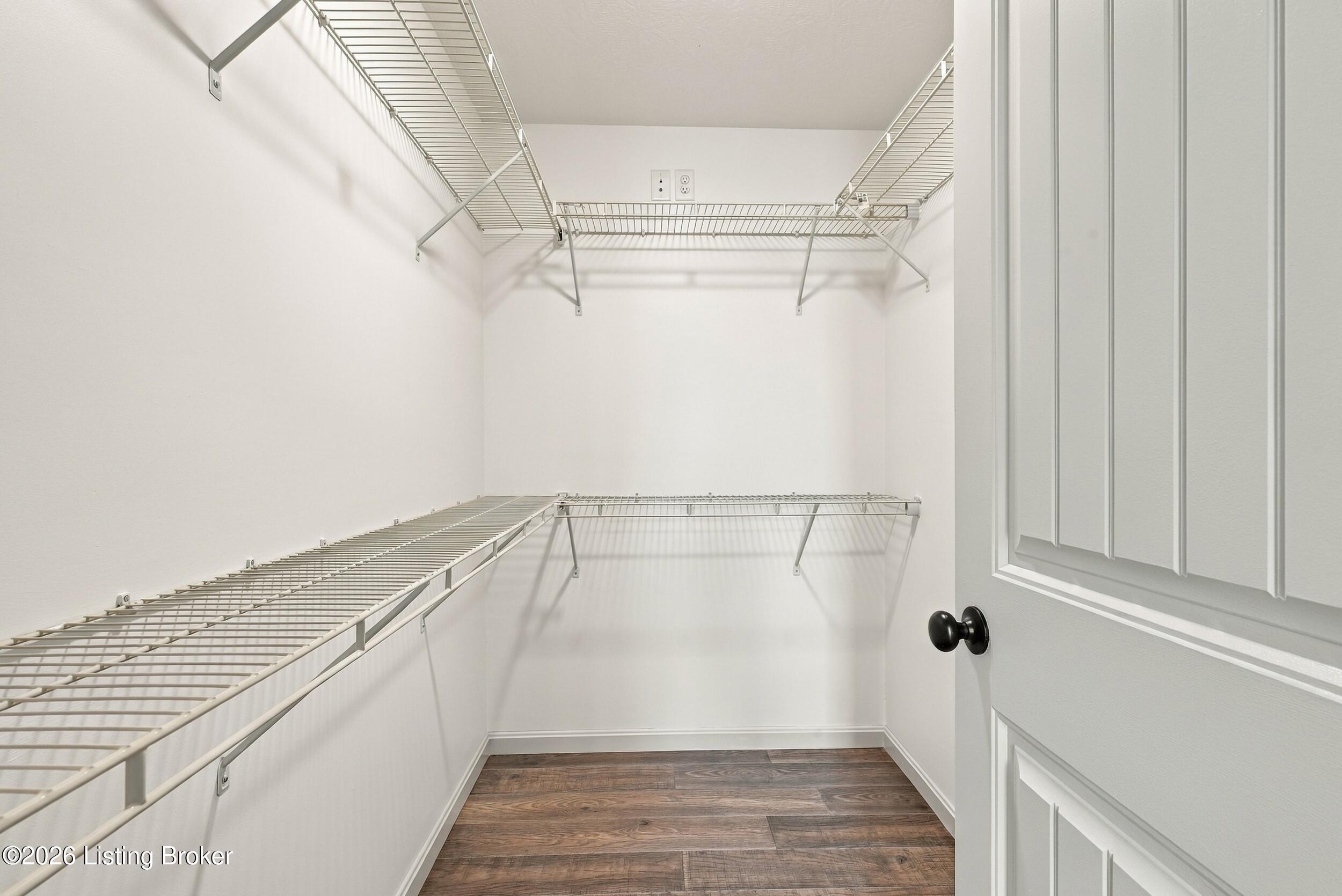 Walk-in closet with extensive white wire shelving and dark wood-look flooring.