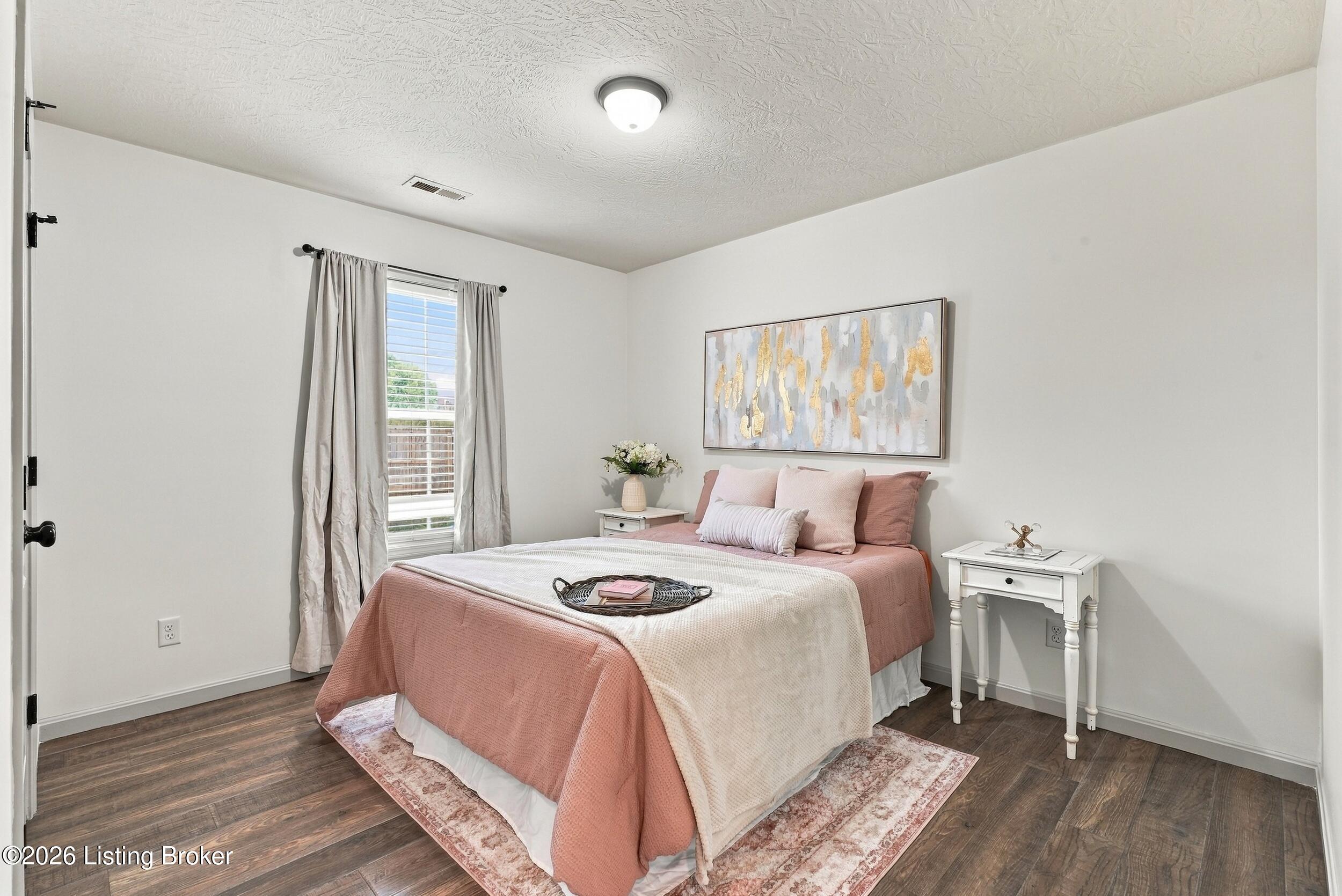 Staged bedroom with blush pink and white bedding, abstract wall art, and a curtained window.