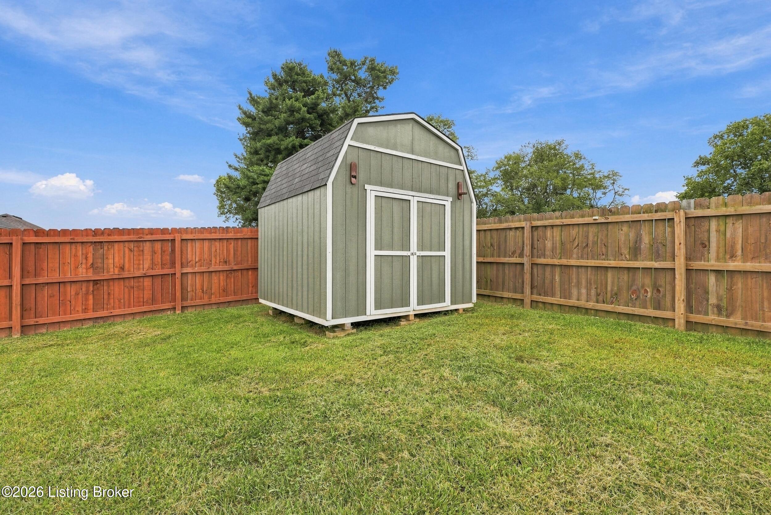 Backyard storage shed with white trim, grassy lawn, and wooden privacy fence.