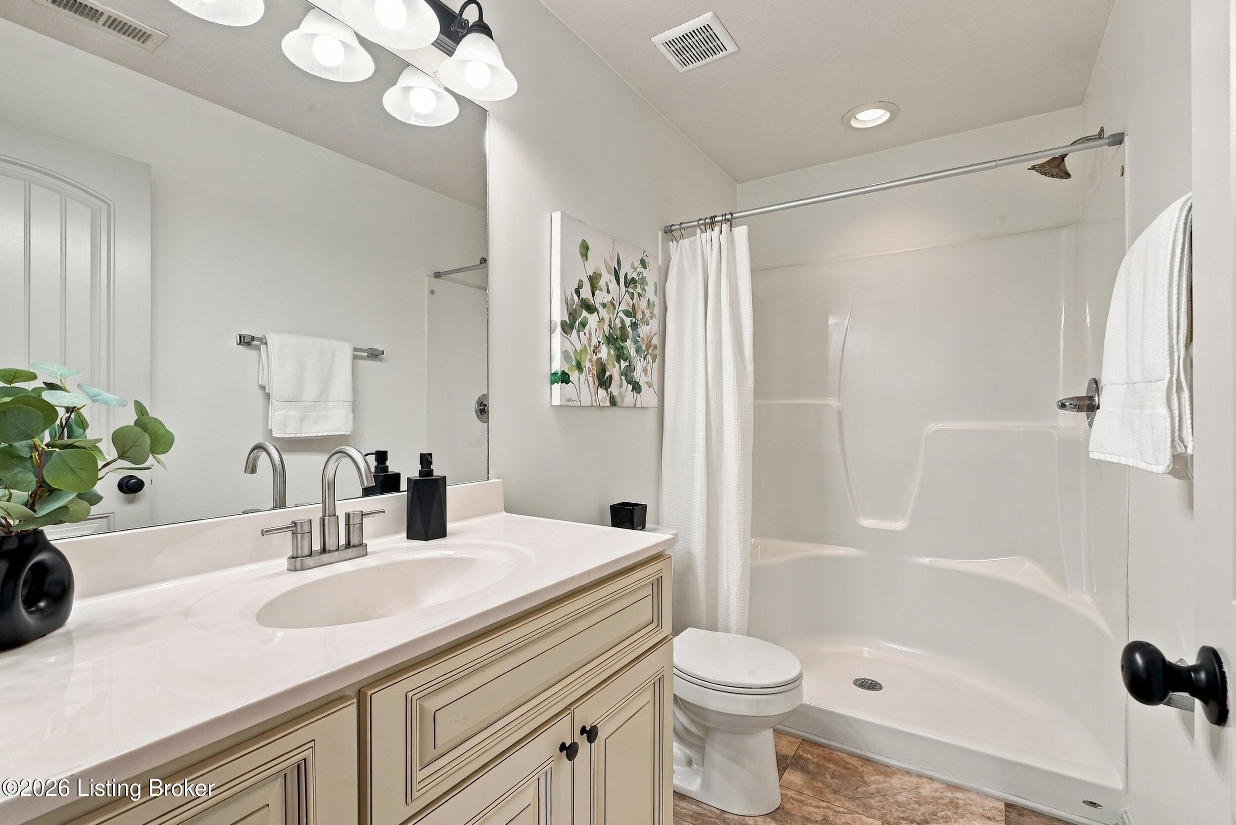Bathroom with beige vanity, white countertop, and tub-shower behind a curtain.