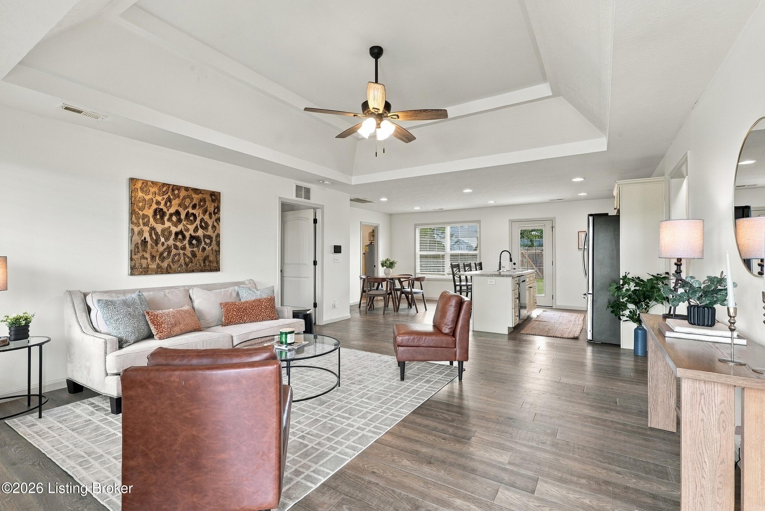 Open-plan living room with tray ceiling, leather chairs, and dining area beside a kitchen island.