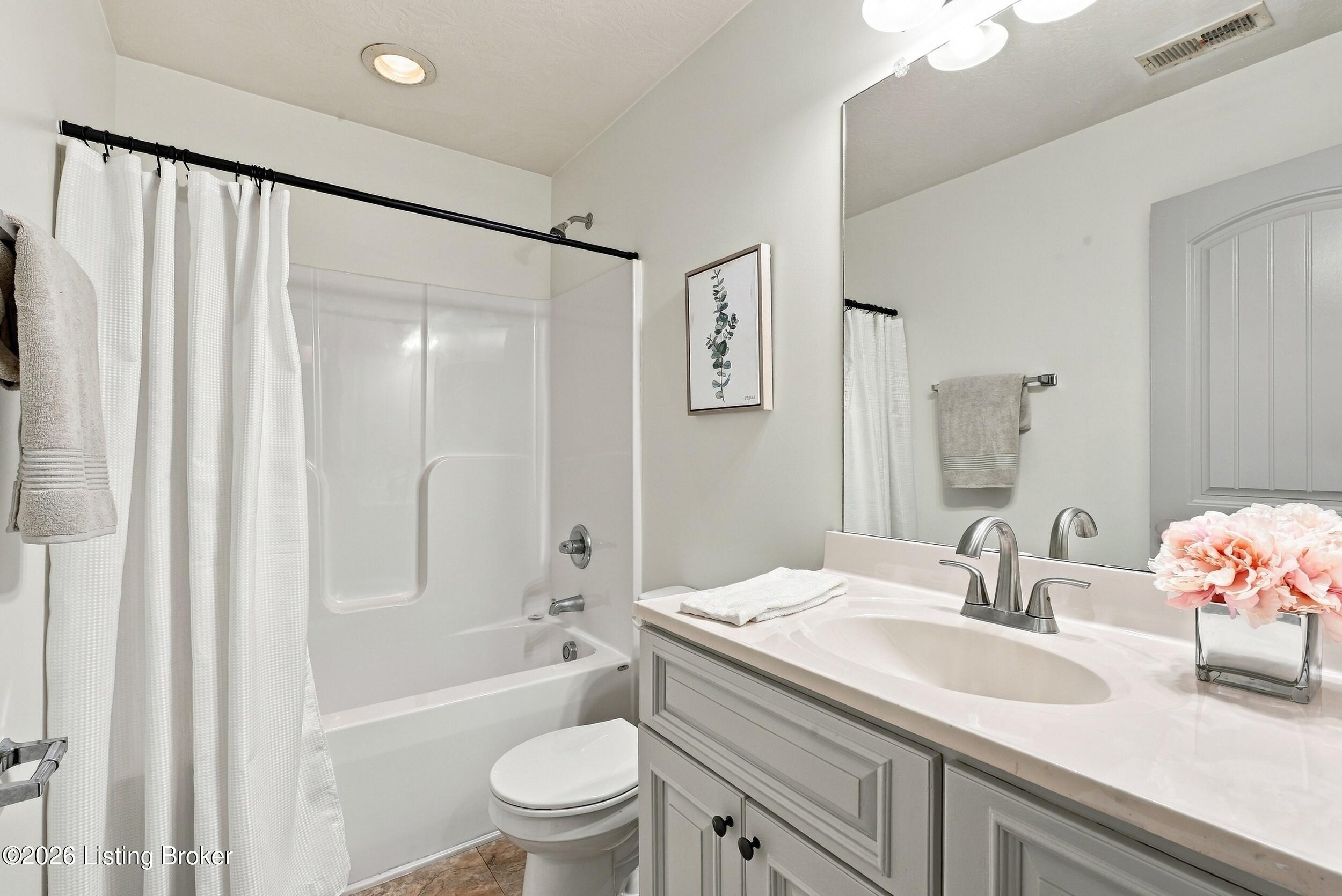 Bathroom with a curtained tub and shower, toilet, and long vanity with a large mirror.