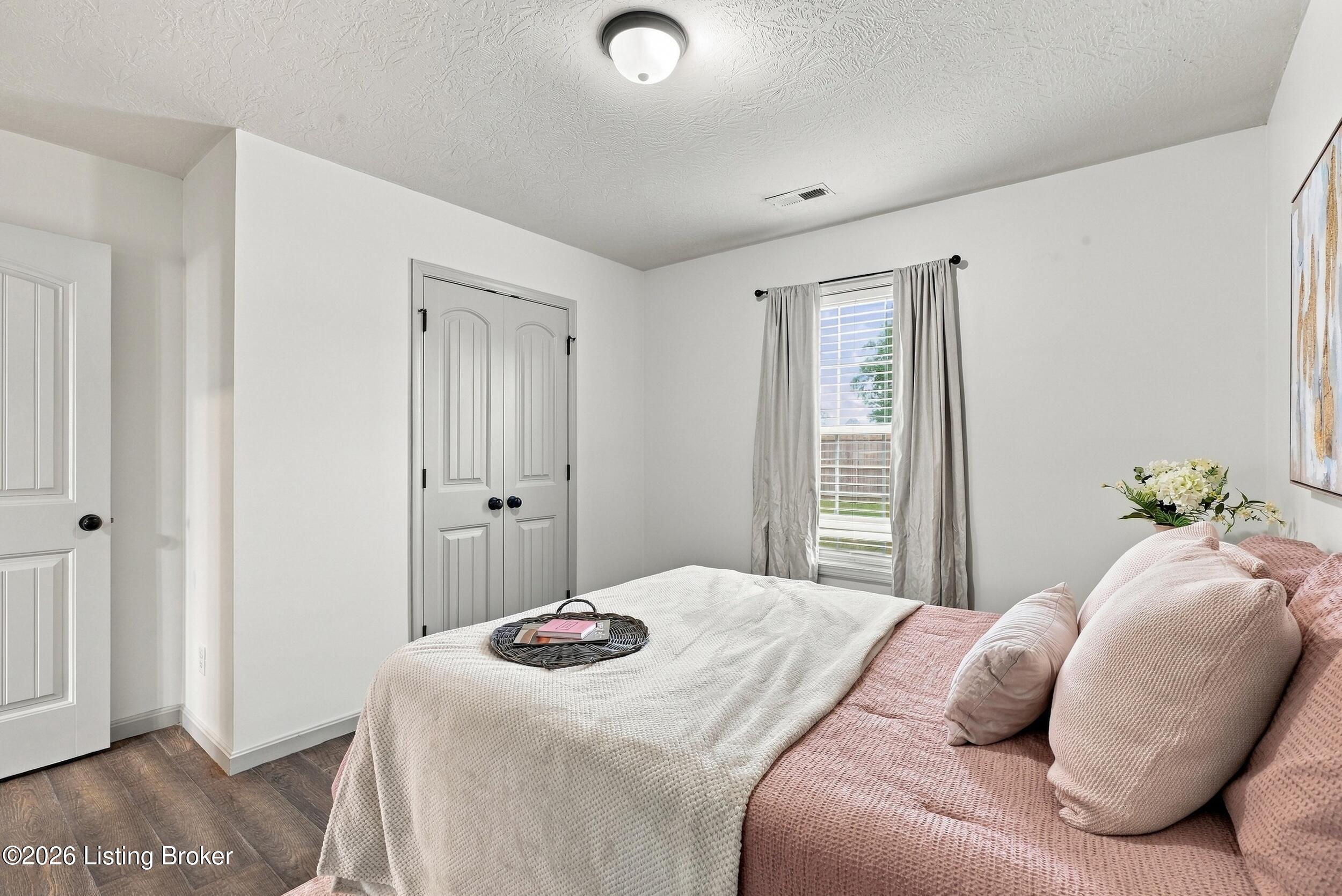 Staged bedroom with a pink bed, white blanket, gray curtains, and double closet doors.