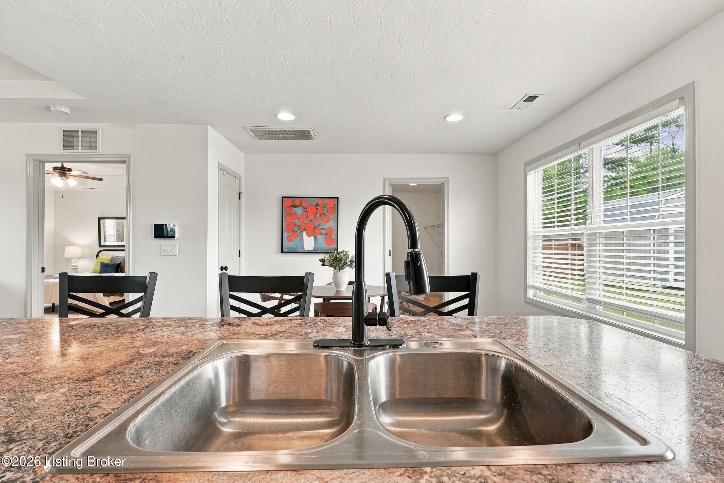 Kitchen sink with black faucet and stone counter overlooking a dining table and large window.