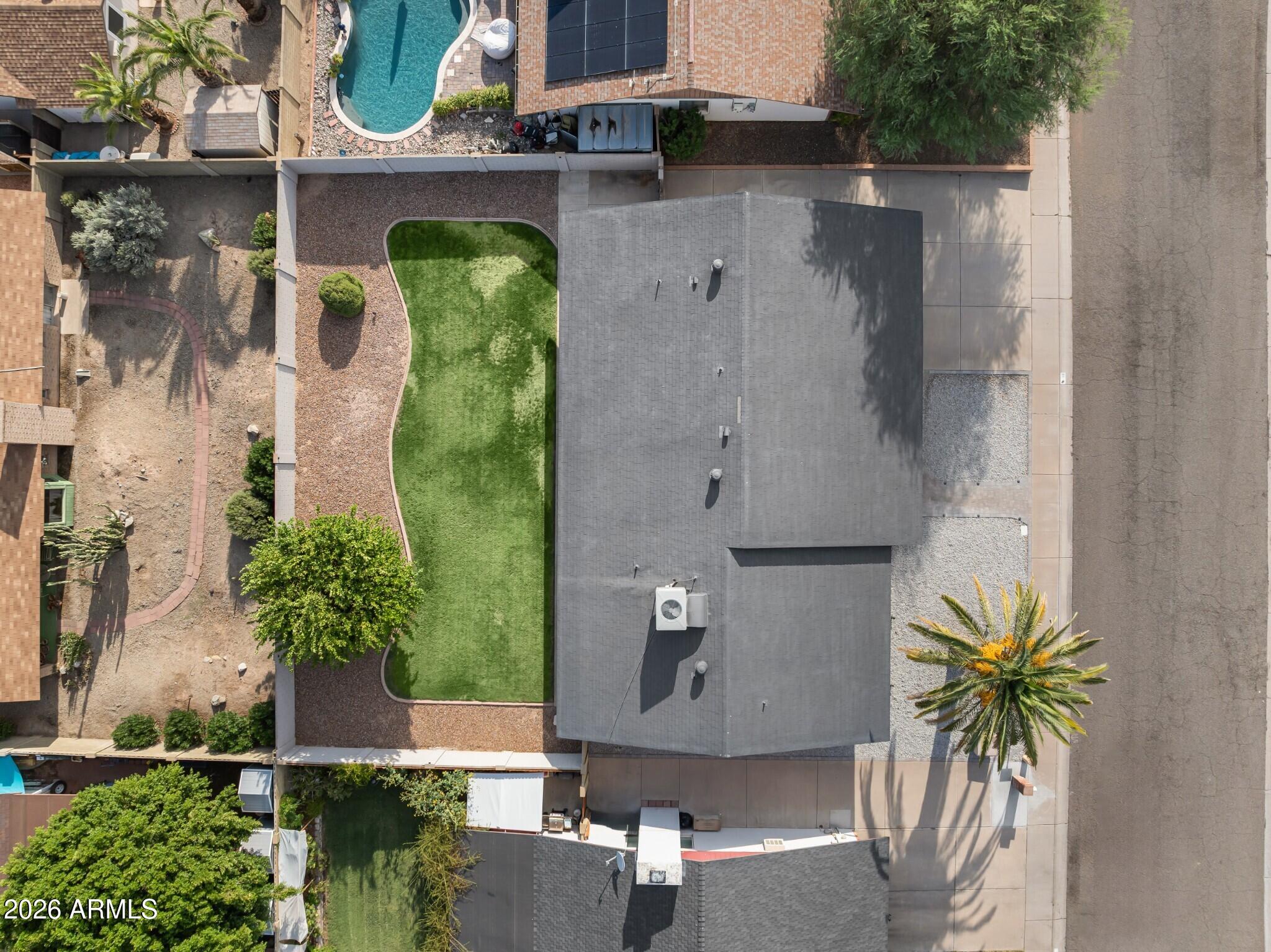 Aerial view of a home with a large gray roof, narrow green lawn, gravel landscaping, and a palm tree.
