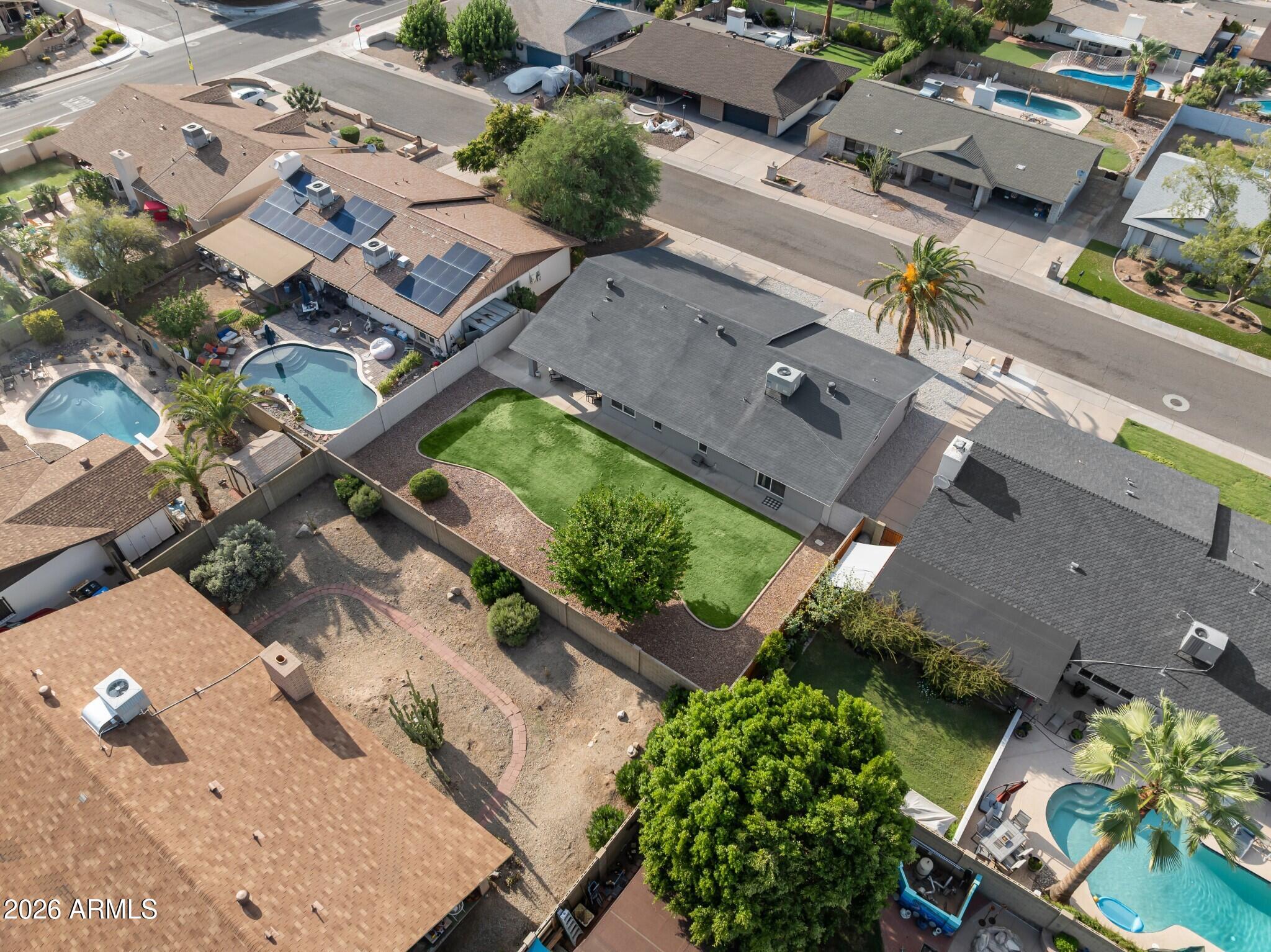 Aerial view of a single-story home with a fenced green lawn and gravel landscaping.