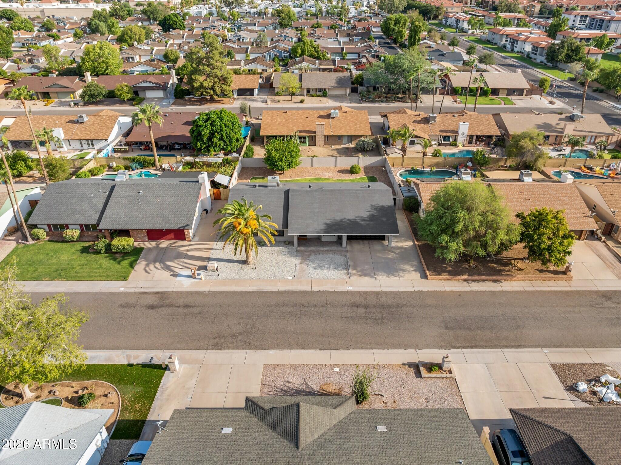 Single-story home with a dark gray roof and gravel front yard, seen from above on a residential street.